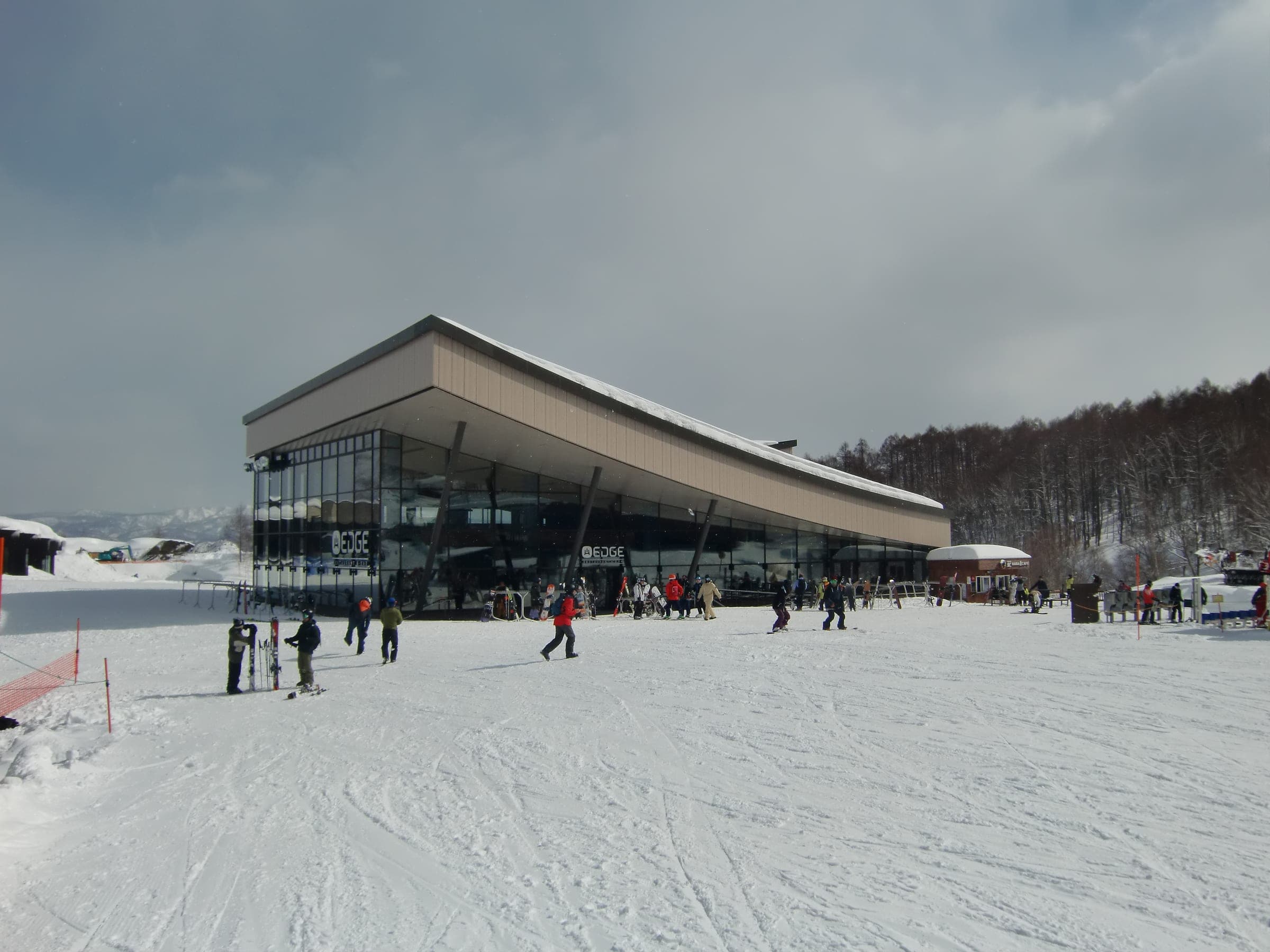 Skiers cross groomed snow below the HANAZONO EDGE building on an overcast day