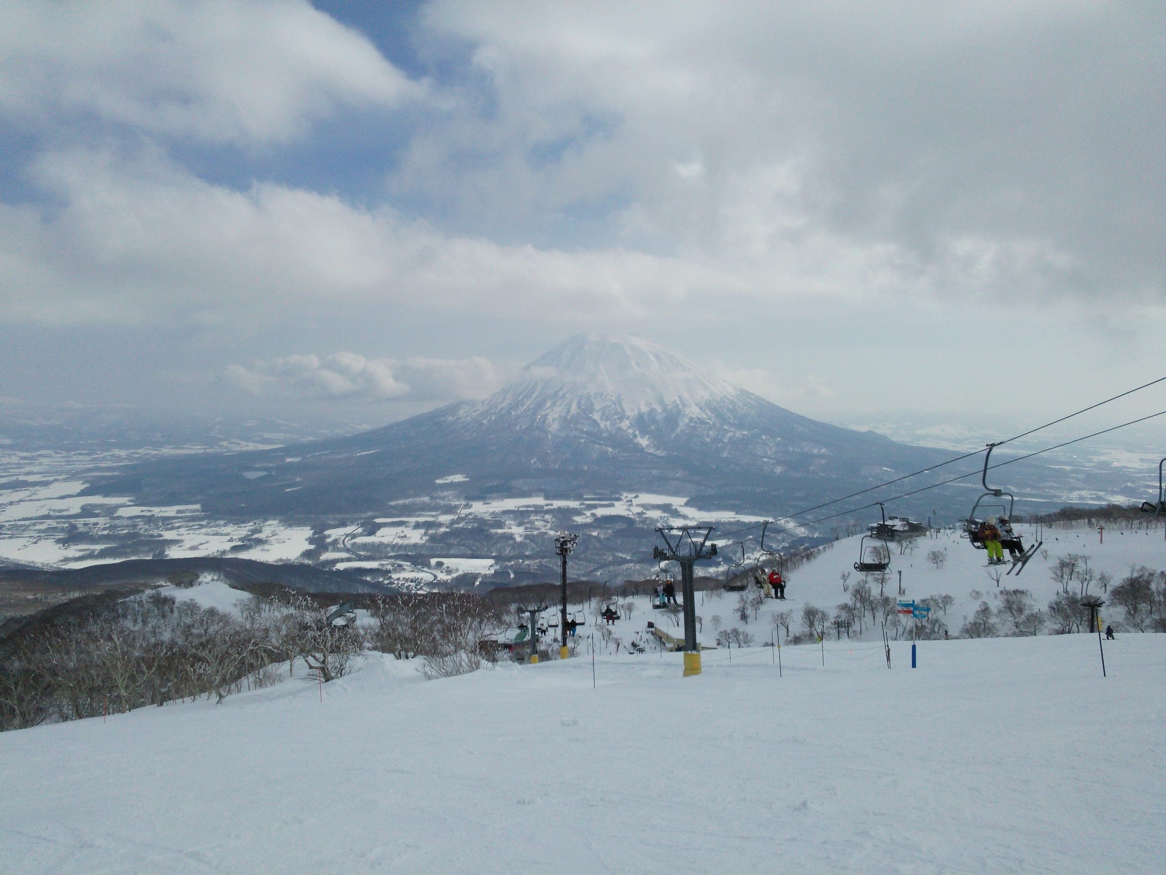 Mt. Yotei rises beyond a chairlift and snowy forest on the slopes of Niseko HANAZONO