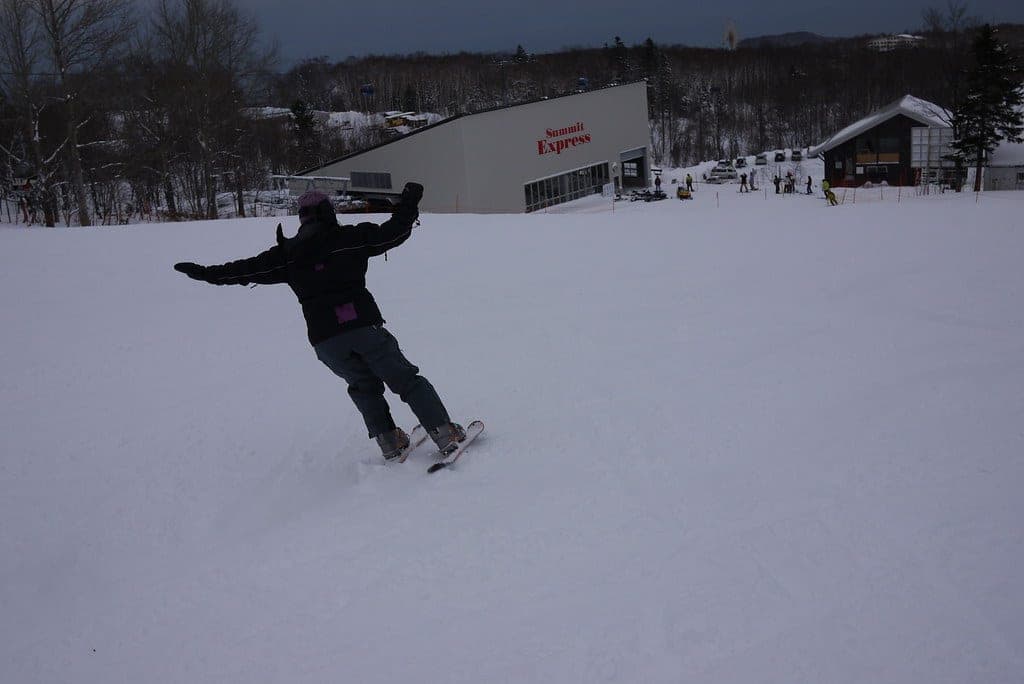 A skier slides across the snow with arms spread near the Highland lodge at Sapporo Teine