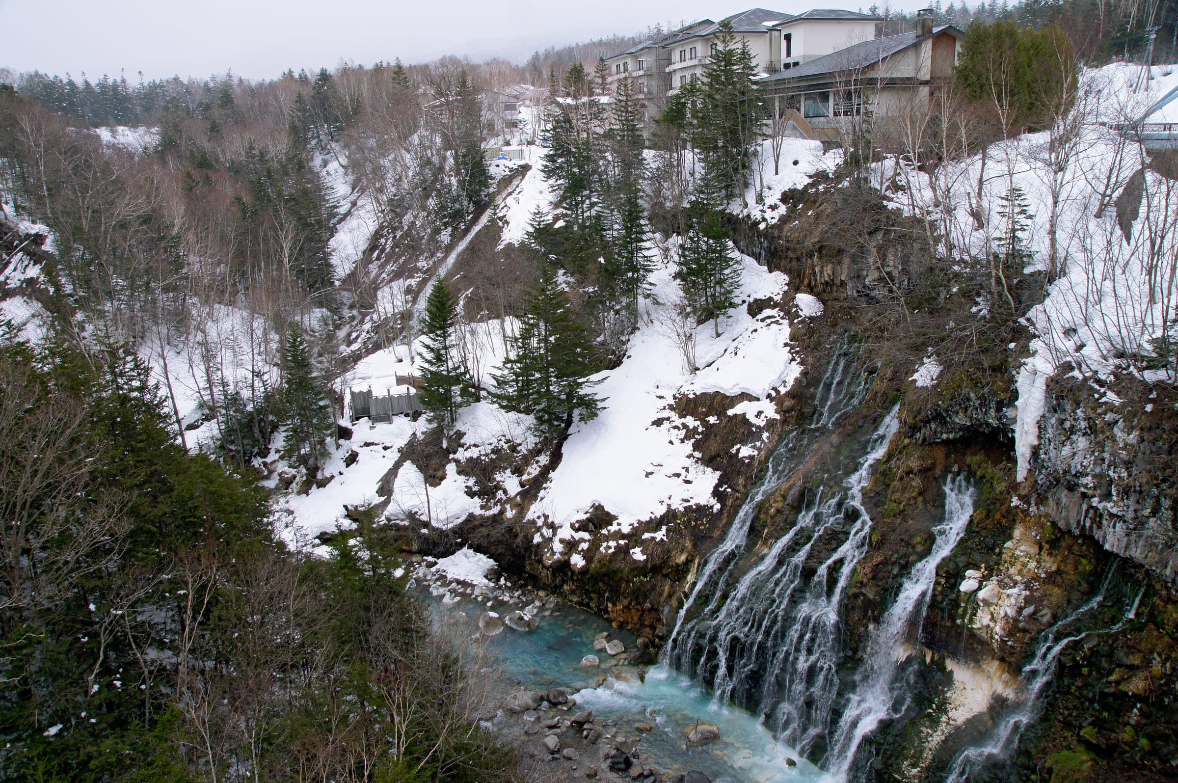 Shirahige Falls pours into the blue Biei River below snowy cliffs a short walk from Aonobi Yuyu