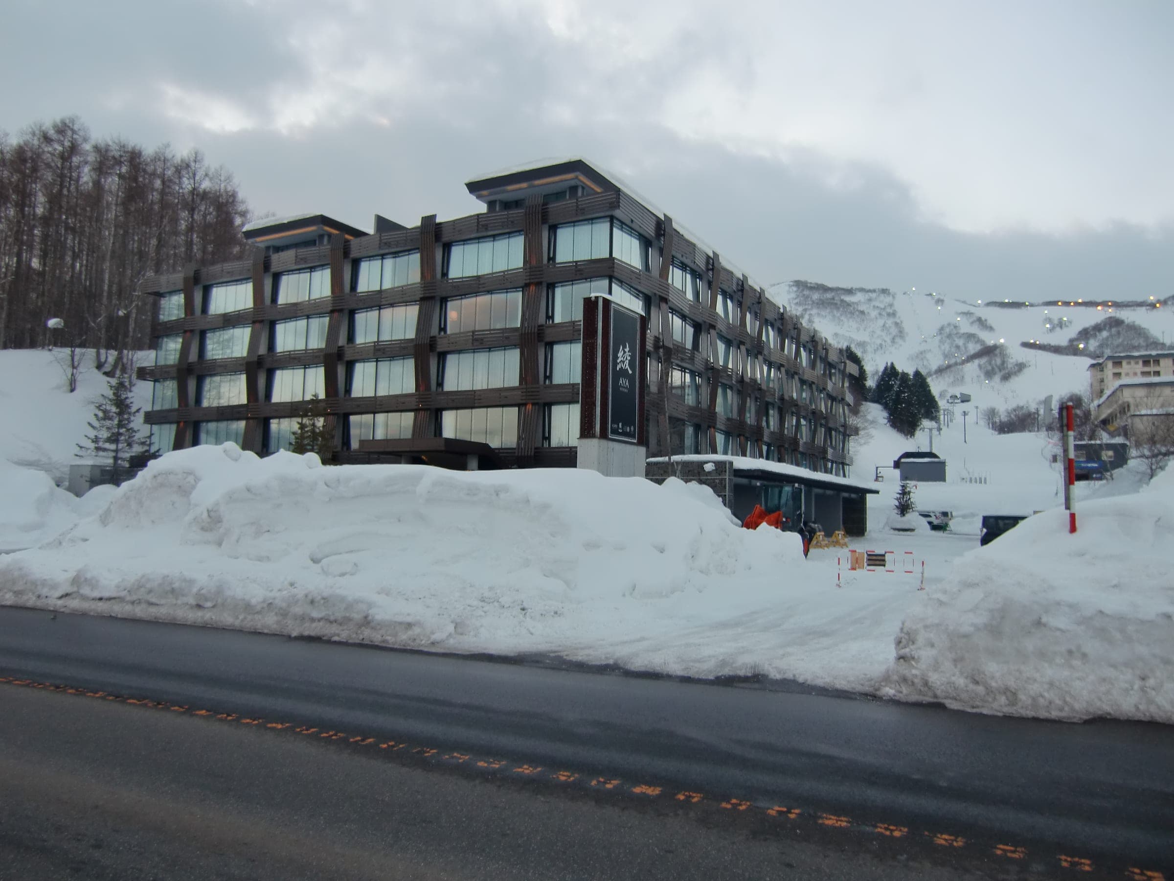 AYA Niseko's dark timber and glass building above roadside snowbanks in Hirafu