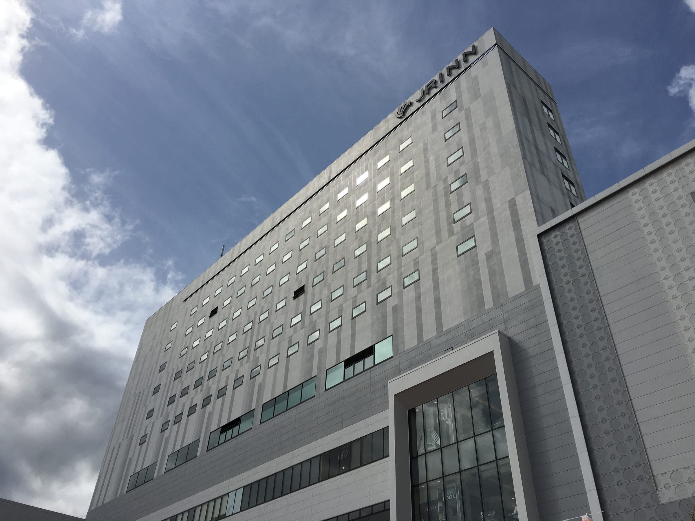 JR Inn Asahikawa's grey glass facade beside Asahikawa Station under a blue sky