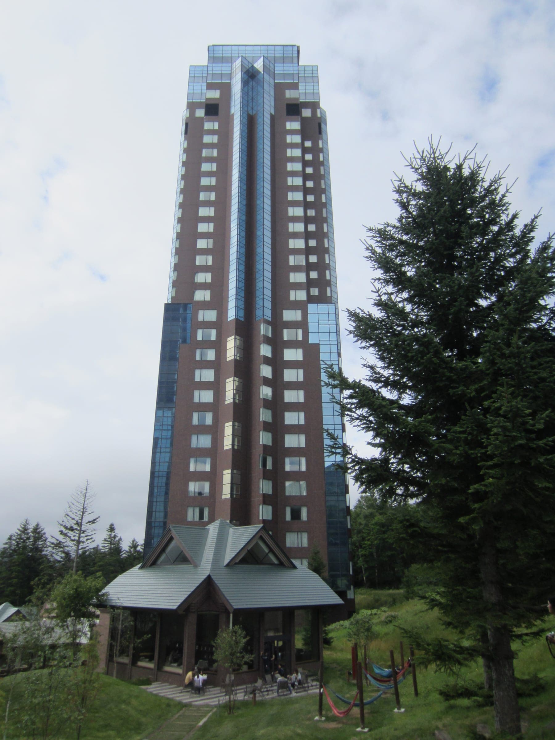 One of RISONARE Tomamu's dark glass towers beside a tall conifer