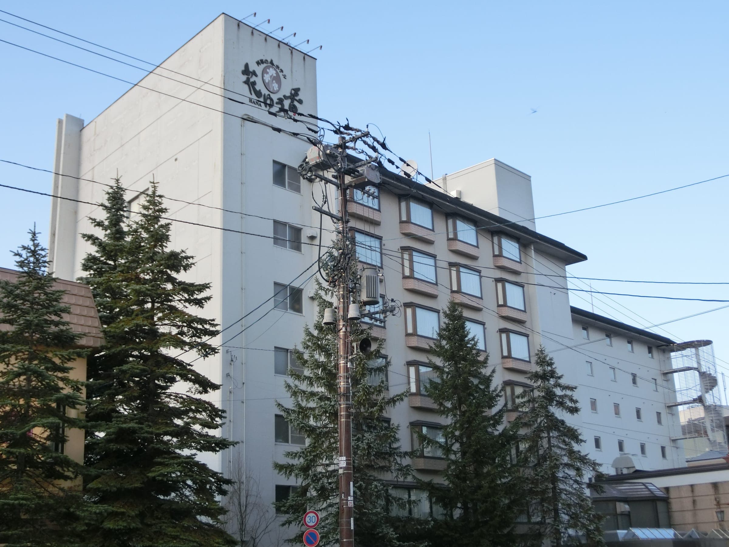 Fir trees stand before the white tower of the former Hanayuuka, now The Forest Akan, in Akanko Onsen