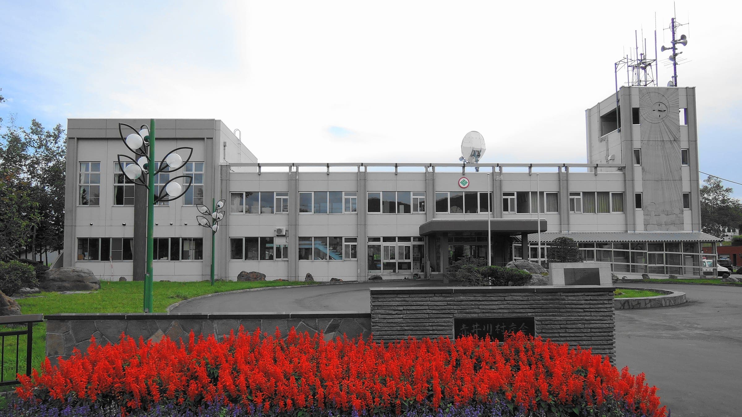 A clock tower rises over Akaigawa village hall behind a bed of red flowers