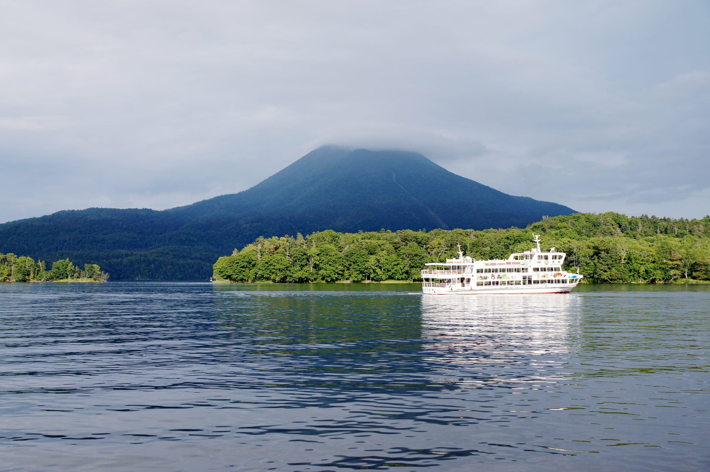 Mt. Oakan rises over Lake Akan as a sightseeing boat passes a wooded island