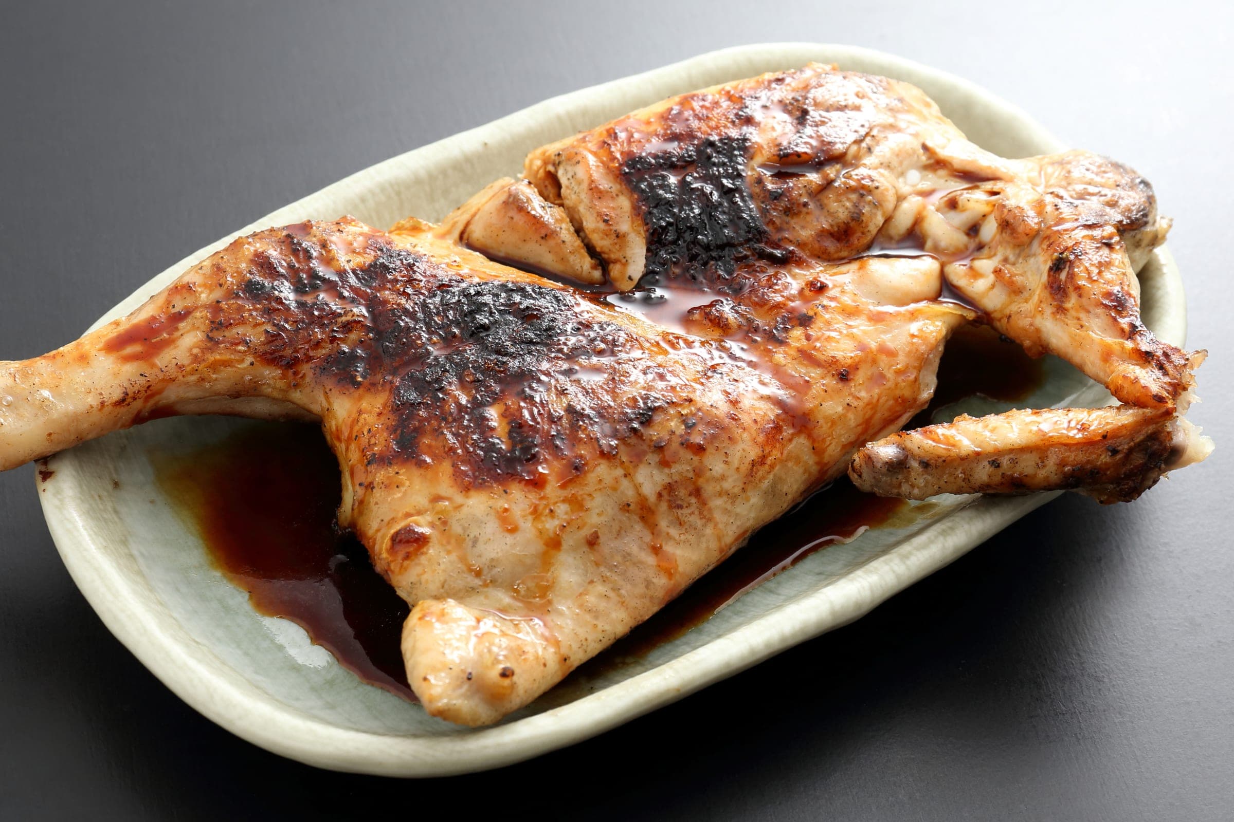 Shinkoyaki, a grilled half chicken with black pepper, on a plate at Ginneko