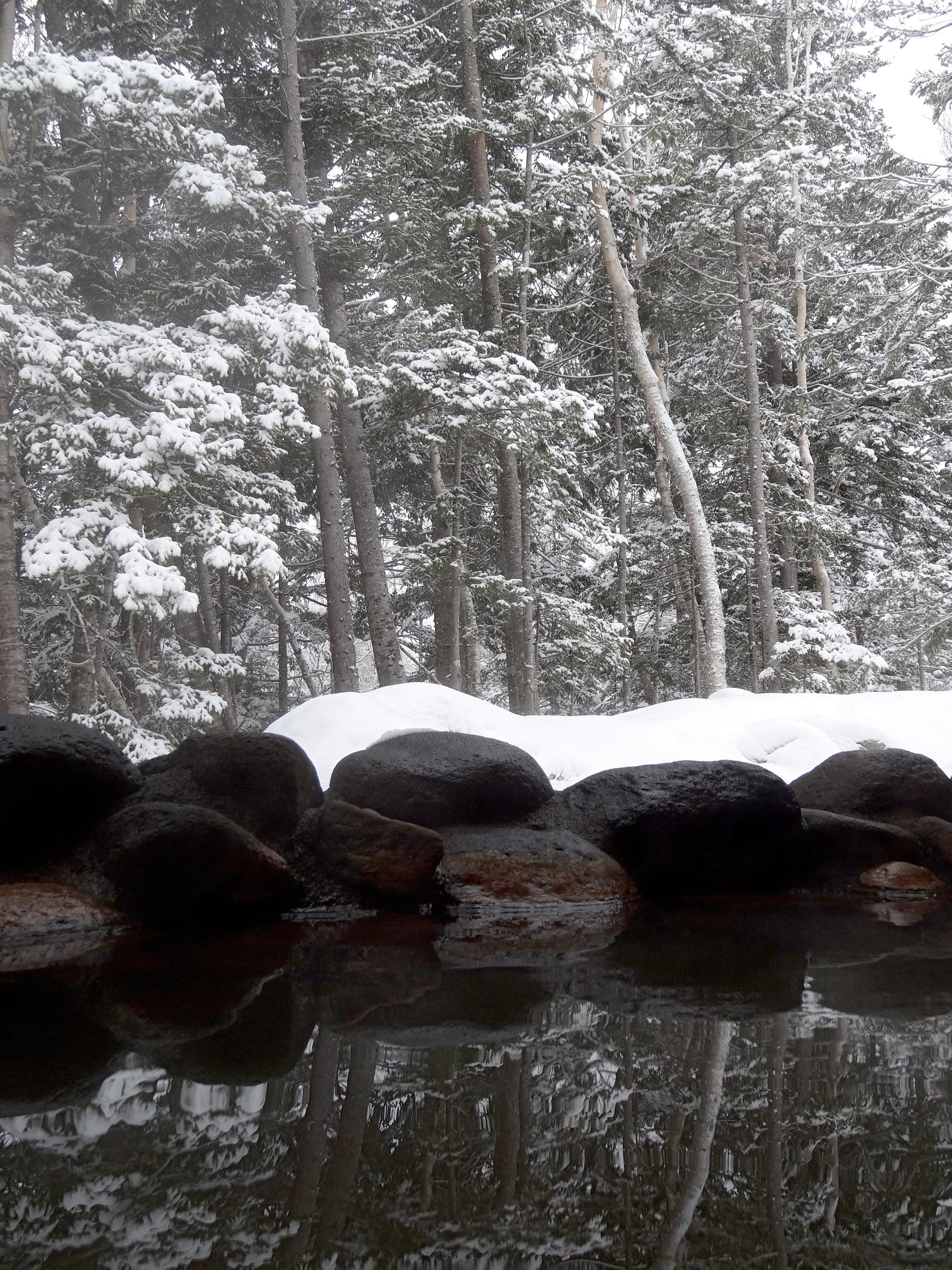 Snow caps the rocks around an outdoor bath at a ryokan in Shirogane Onsen