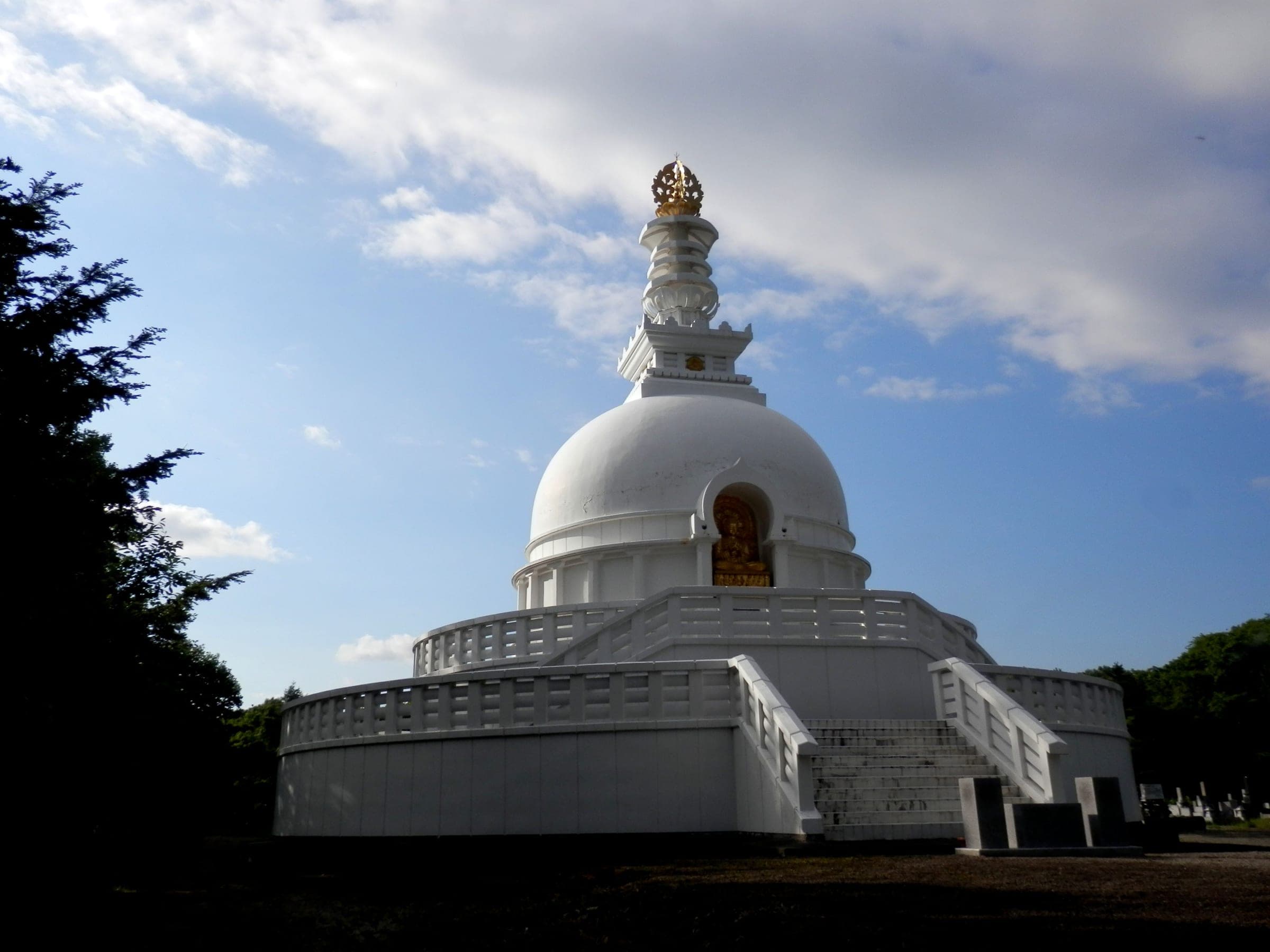 The white Chitose Stupa rises above dark pines in Rankoshi Cemetery under a blue sky