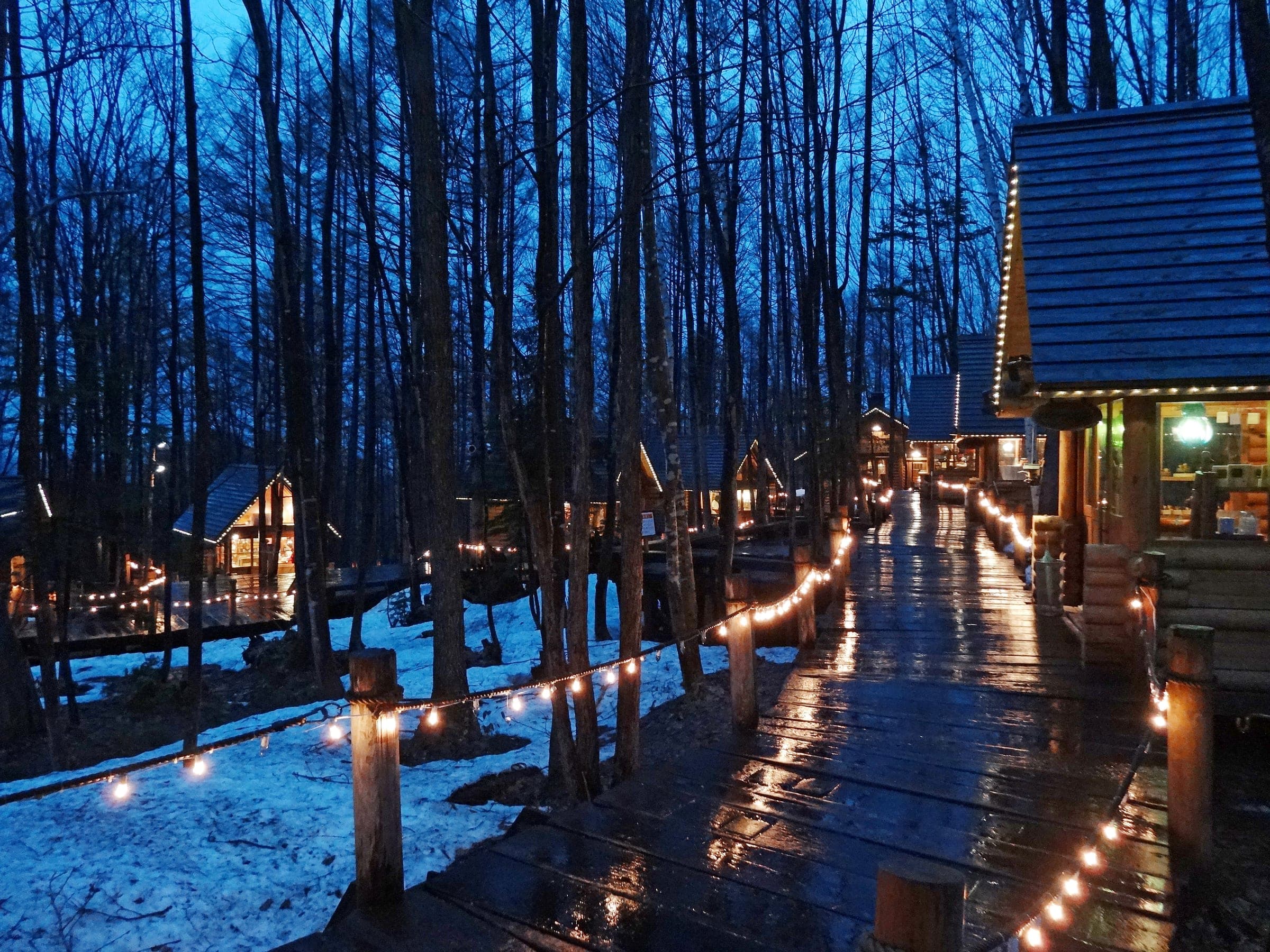 Lights trace the boardwalk between log cabin shops at Ningle Terrace in the snow