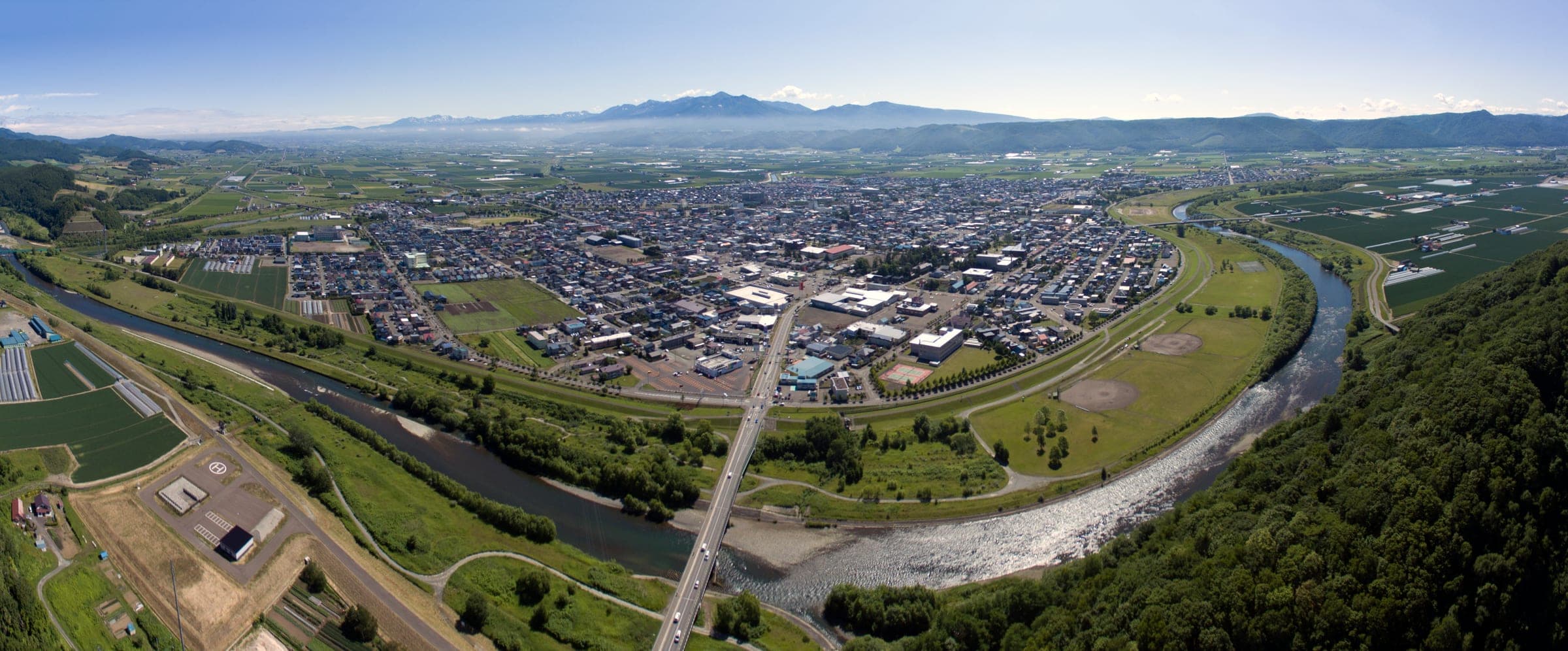 Aerial view of Furano spread across the valley floor beside a river, with mountains on the horizon