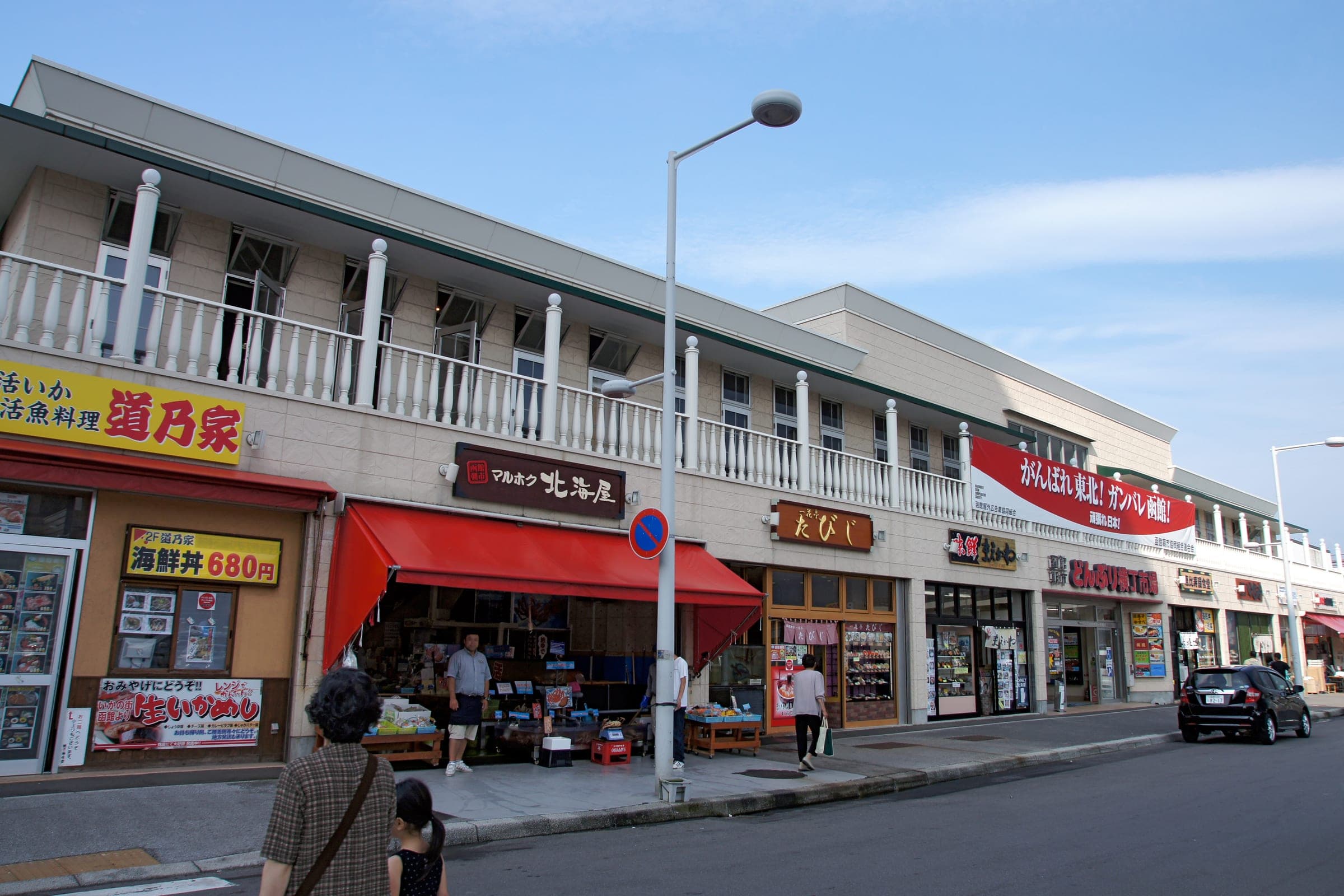 Shopfronts with red awnings line a street at the Hakodate Morning Market under a clear sky
