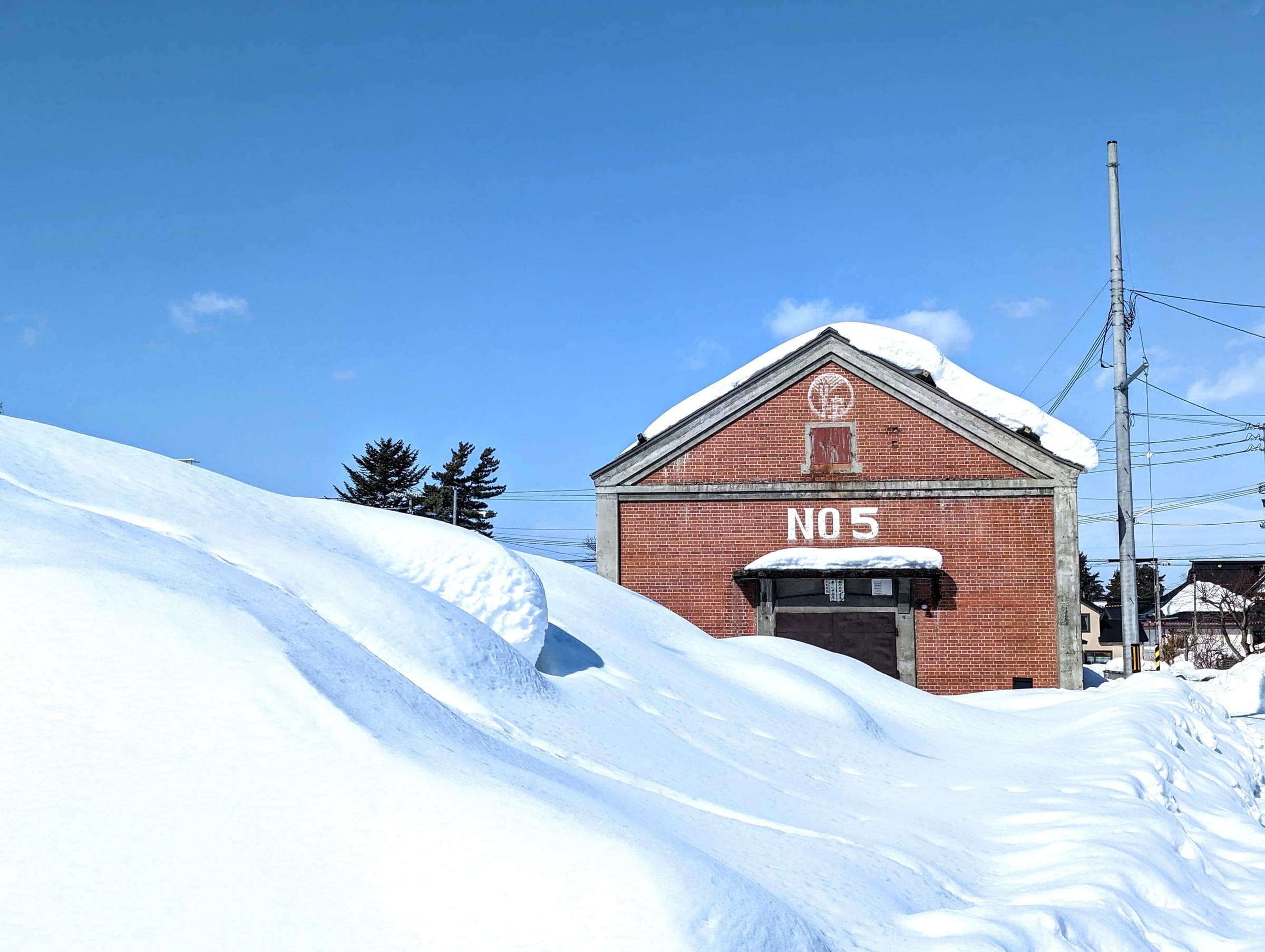 A red brick warehouse marked No5 sits in deep snow in Higashikawa under a blue sky