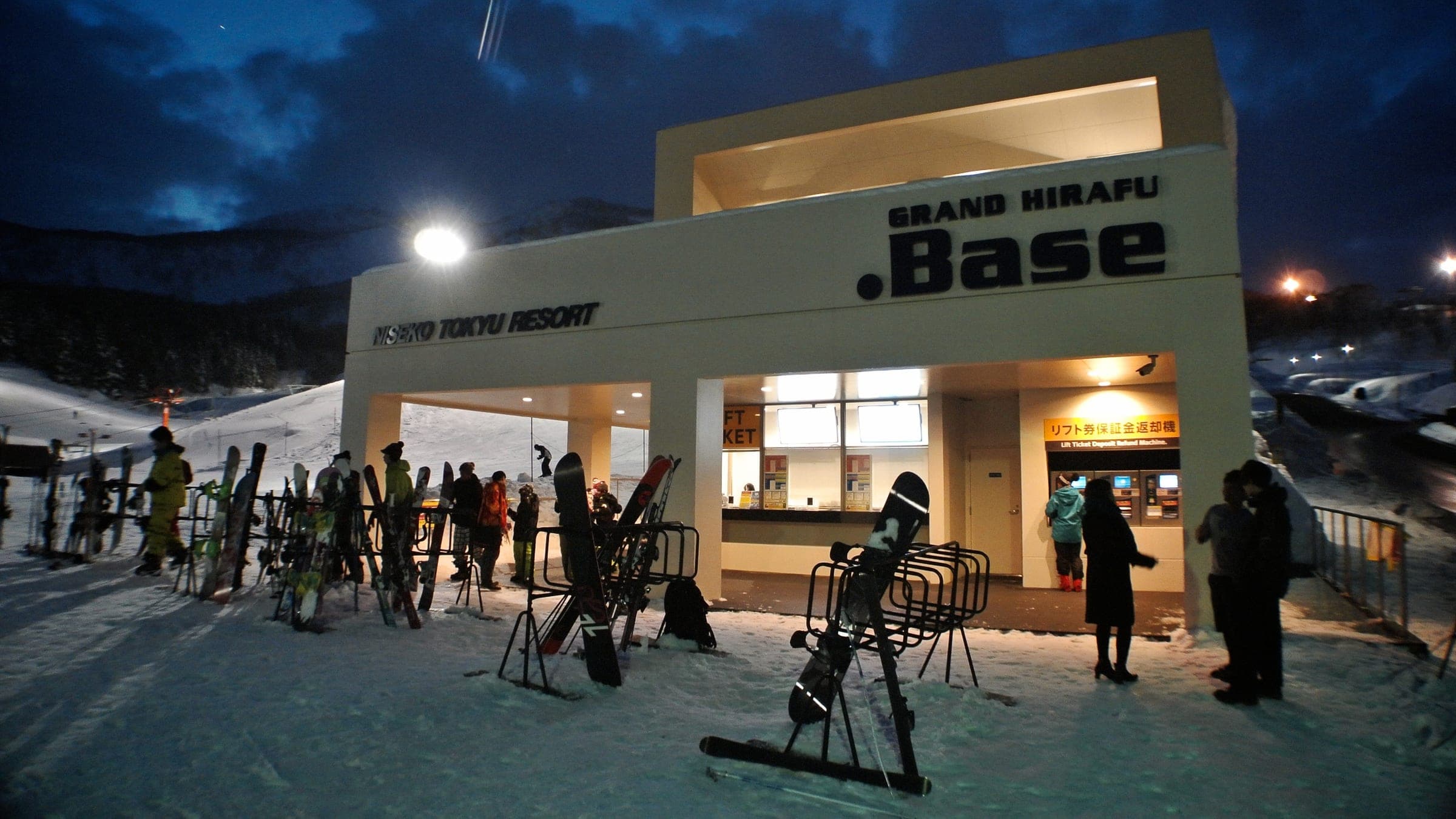 Skis stand in racks outside the lit Grand Hirafu .Base building on a winter evening