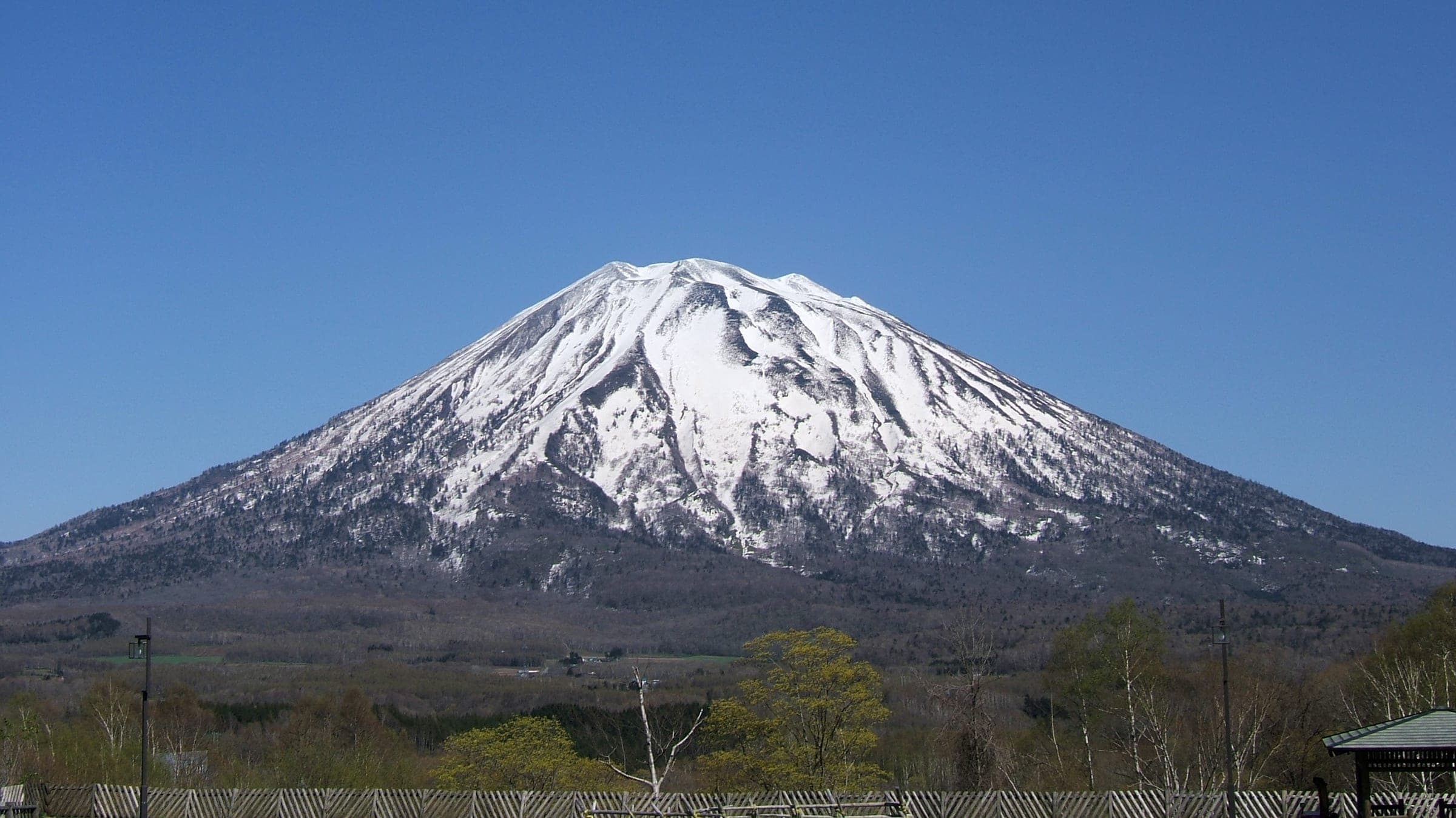 Mount Yotei's snow-capped cone rises above dark forest in the view from Hirafu