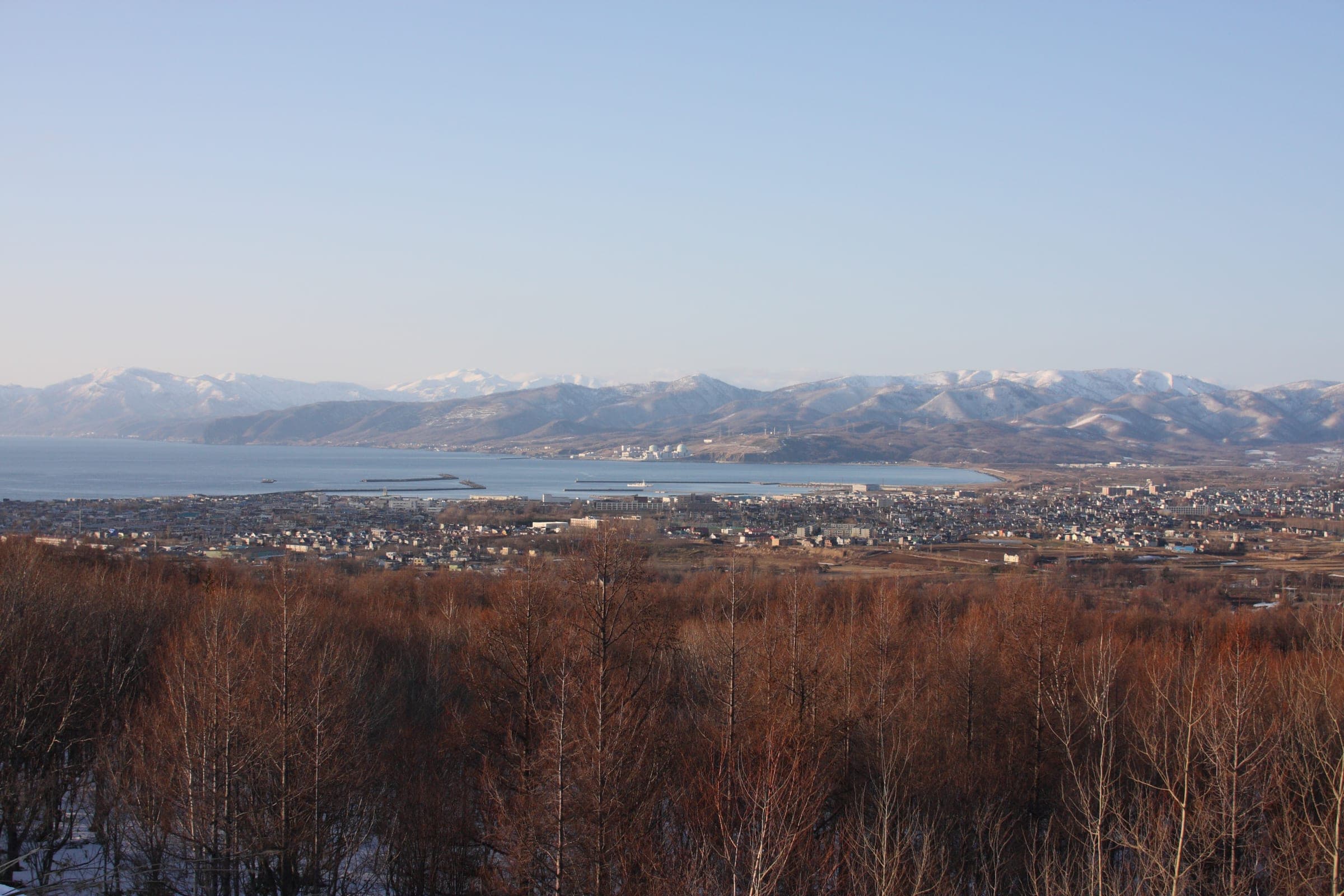 Iwanai and the sea seen across brown fields, with snowy peaks along the horizon