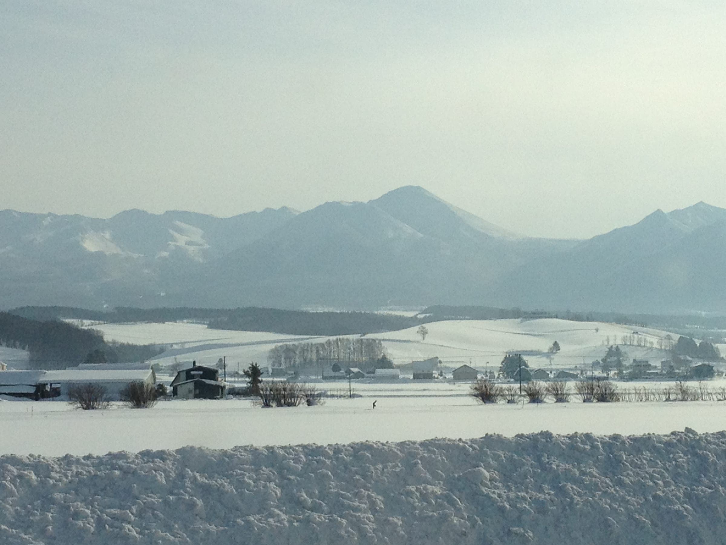 The snow-covered Tokachi-dake range rises behind winter farmland near Kamifurano