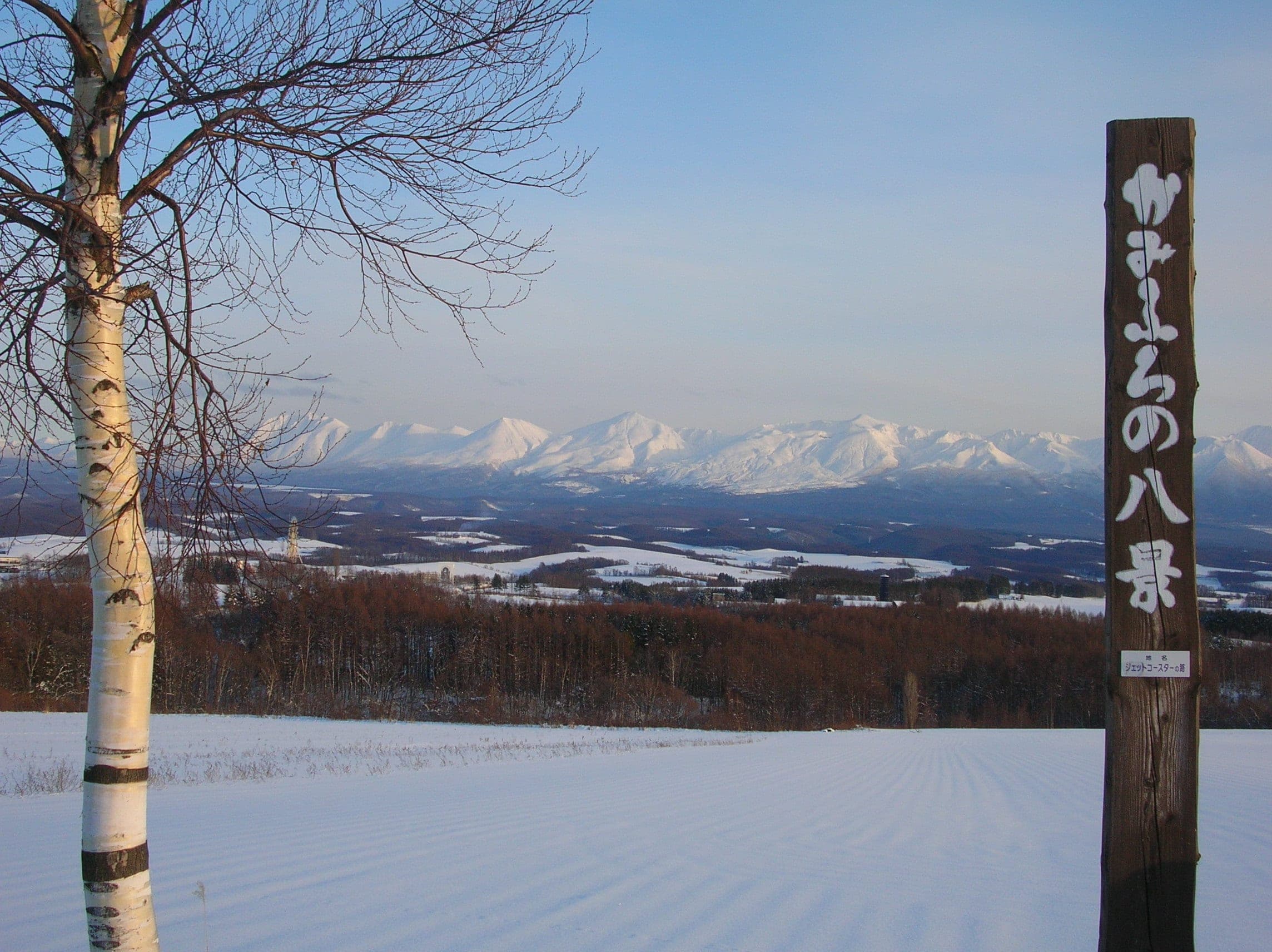 Snowy fields and birch trees face the white Tokachi range from a Kamifurano viewpoint