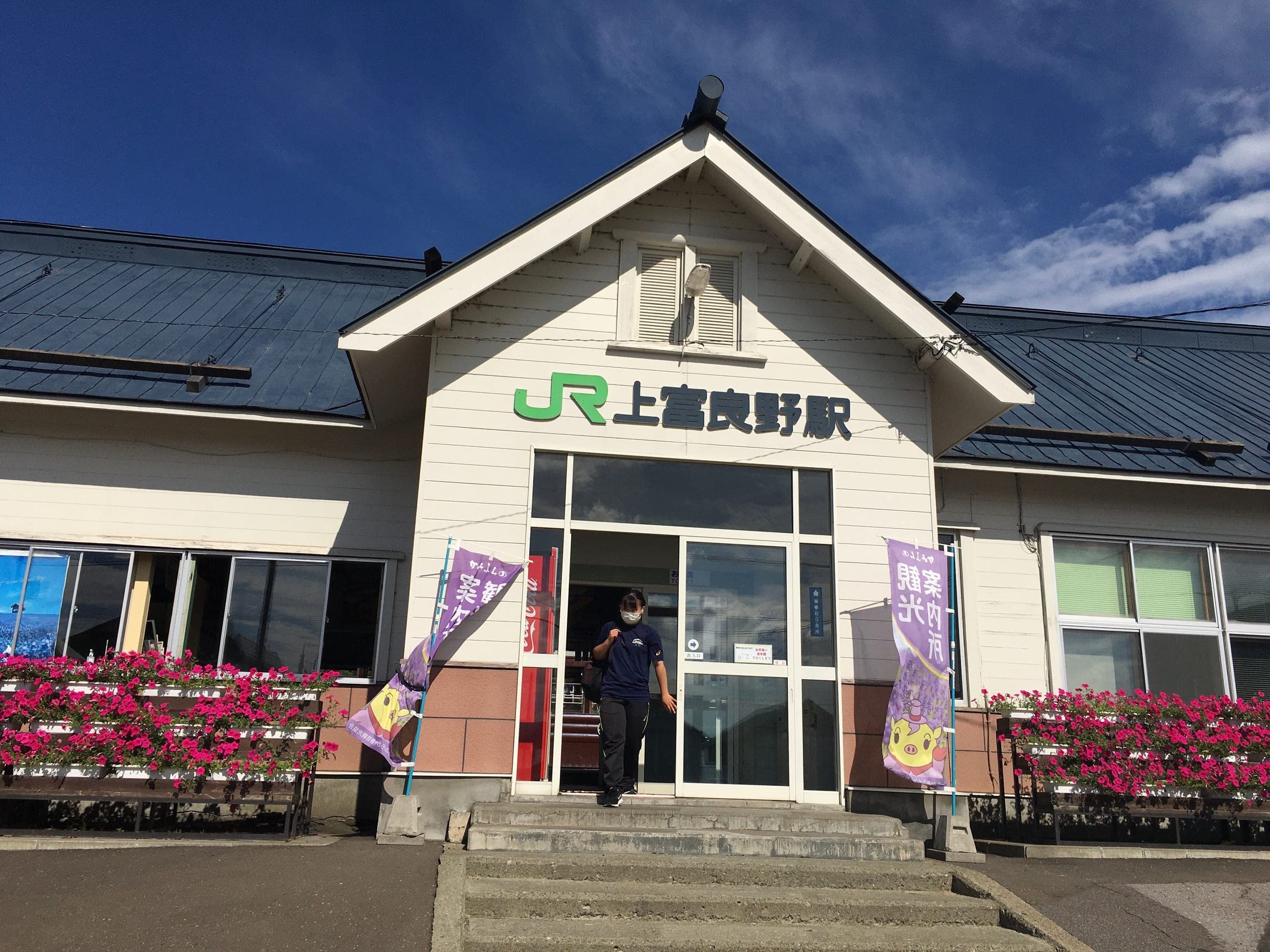 The gabled front of Kami-Furano Station with flower boxes under a blue summer sky