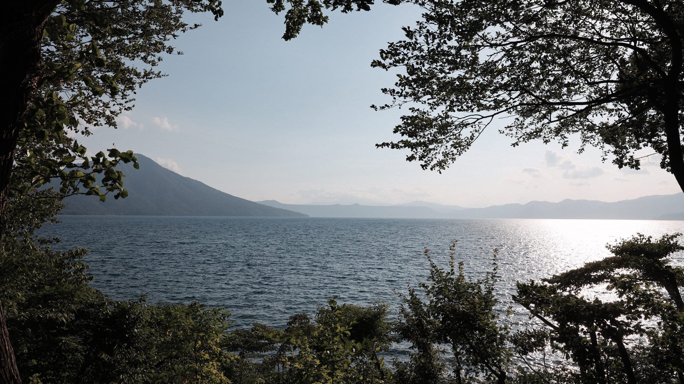 Lake Shikotsu seen through lakeside trees in hazy afternoon light