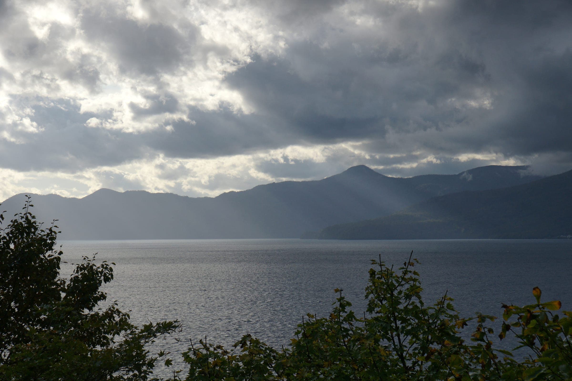 Sunlight breaks through storm clouds over Lake Shikotsu and Mt. Ninaru