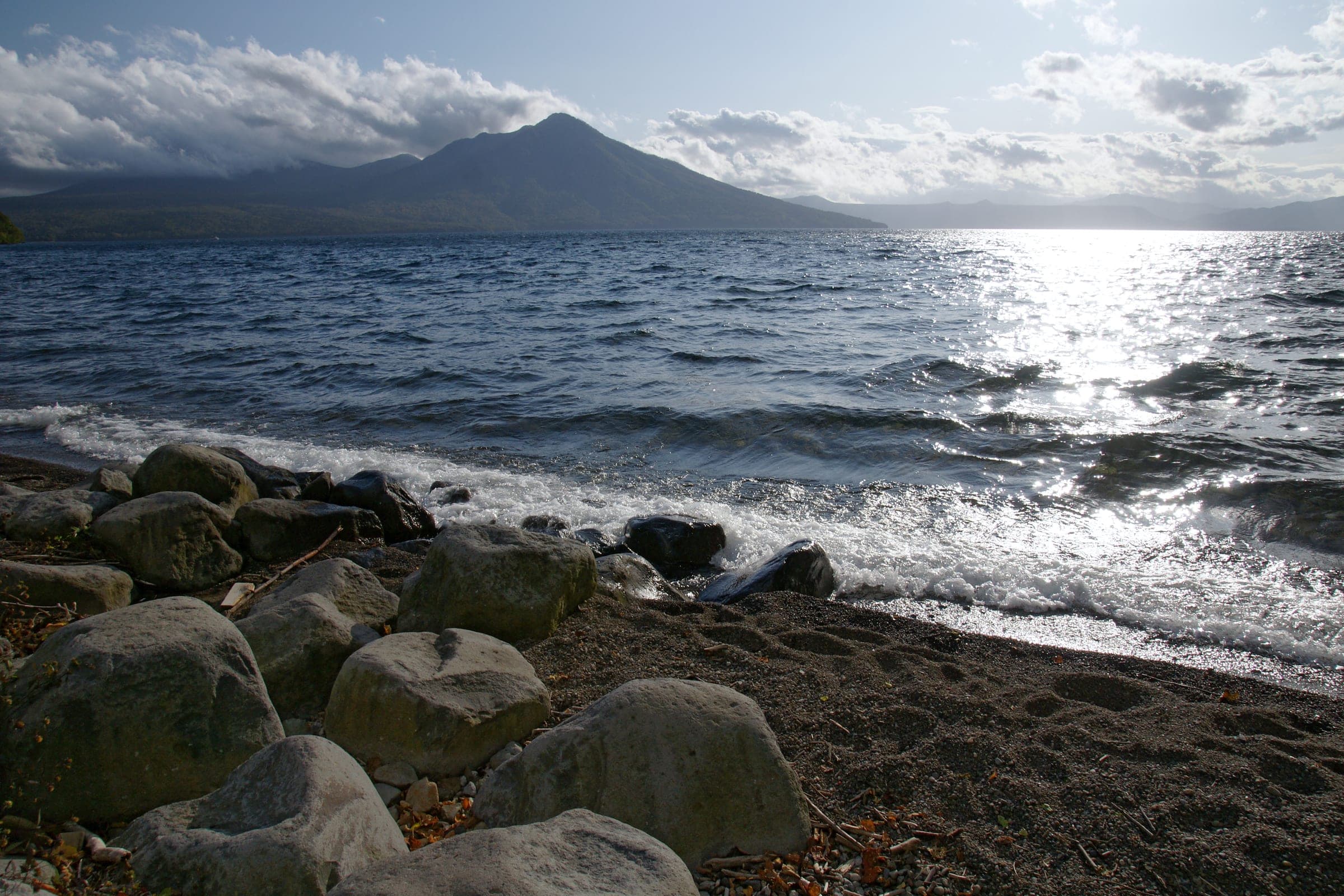 Waves wash over the rocky shore of Lake Shikotsu toward Mt. Fuppushi