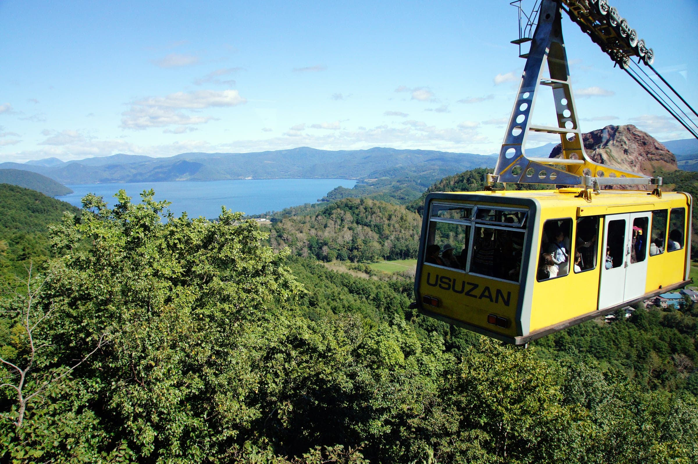 A yellow Usuzan Ropeway cabin climbs Mt. Usu above Lake Toya