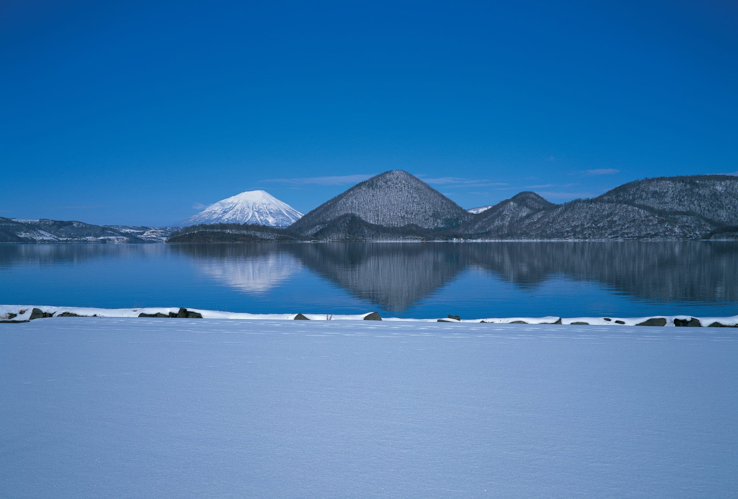 Snowy hills and Mount Yotei reflected in the still water of Lake Toya in winter