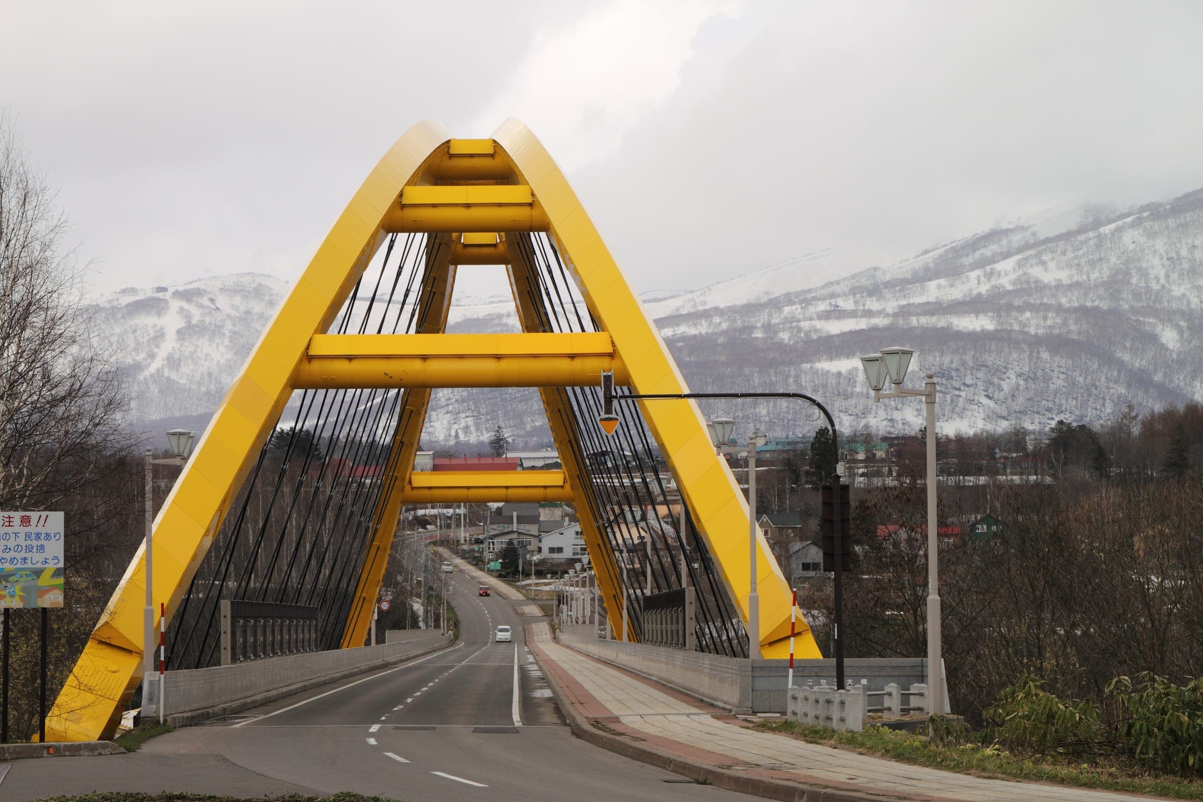 The yellow arch of the Niseko Ohashi bridge with snowy mountains behind