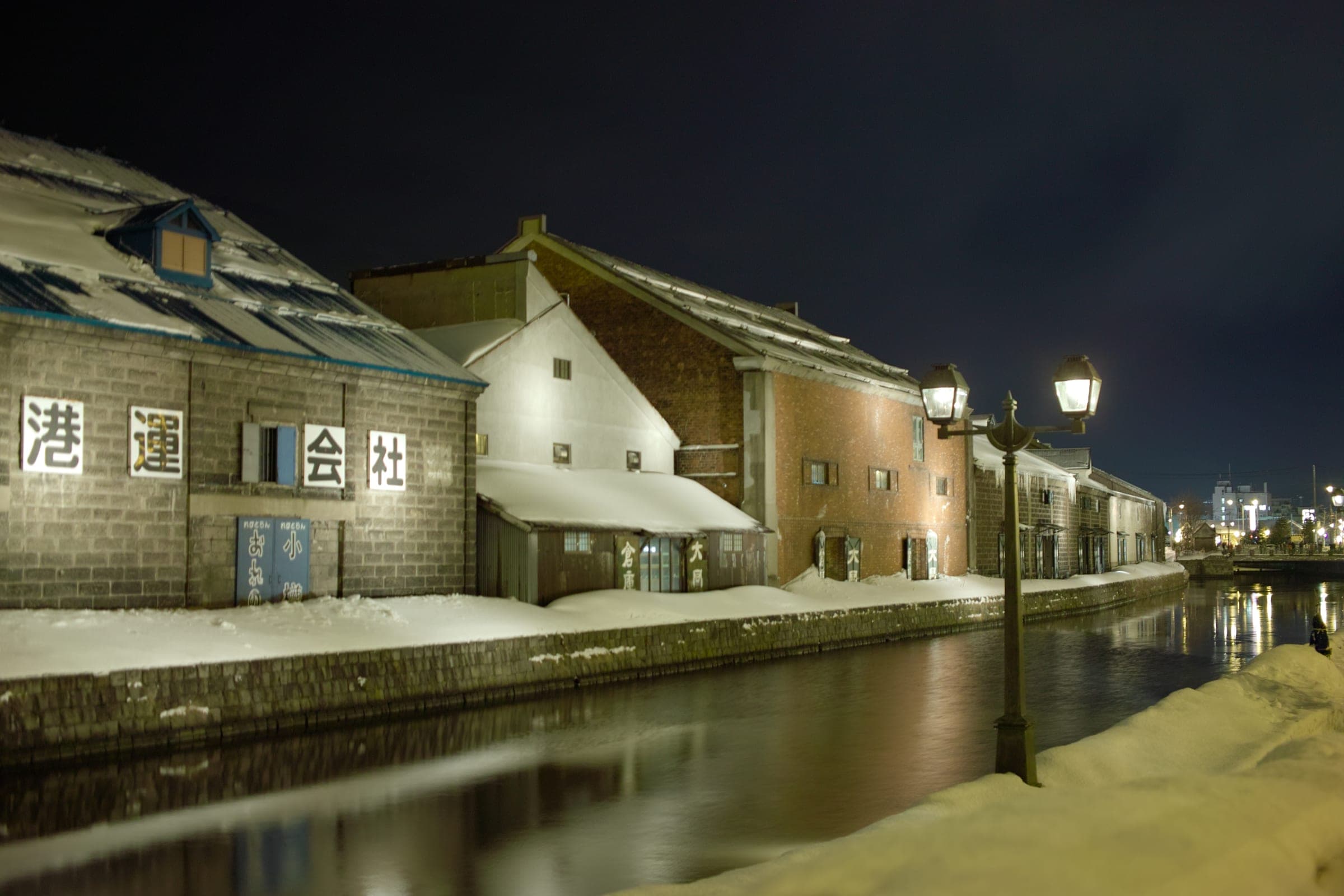 Old stone warehouses and gas lamps along the Otaru Canal at dusk in winter