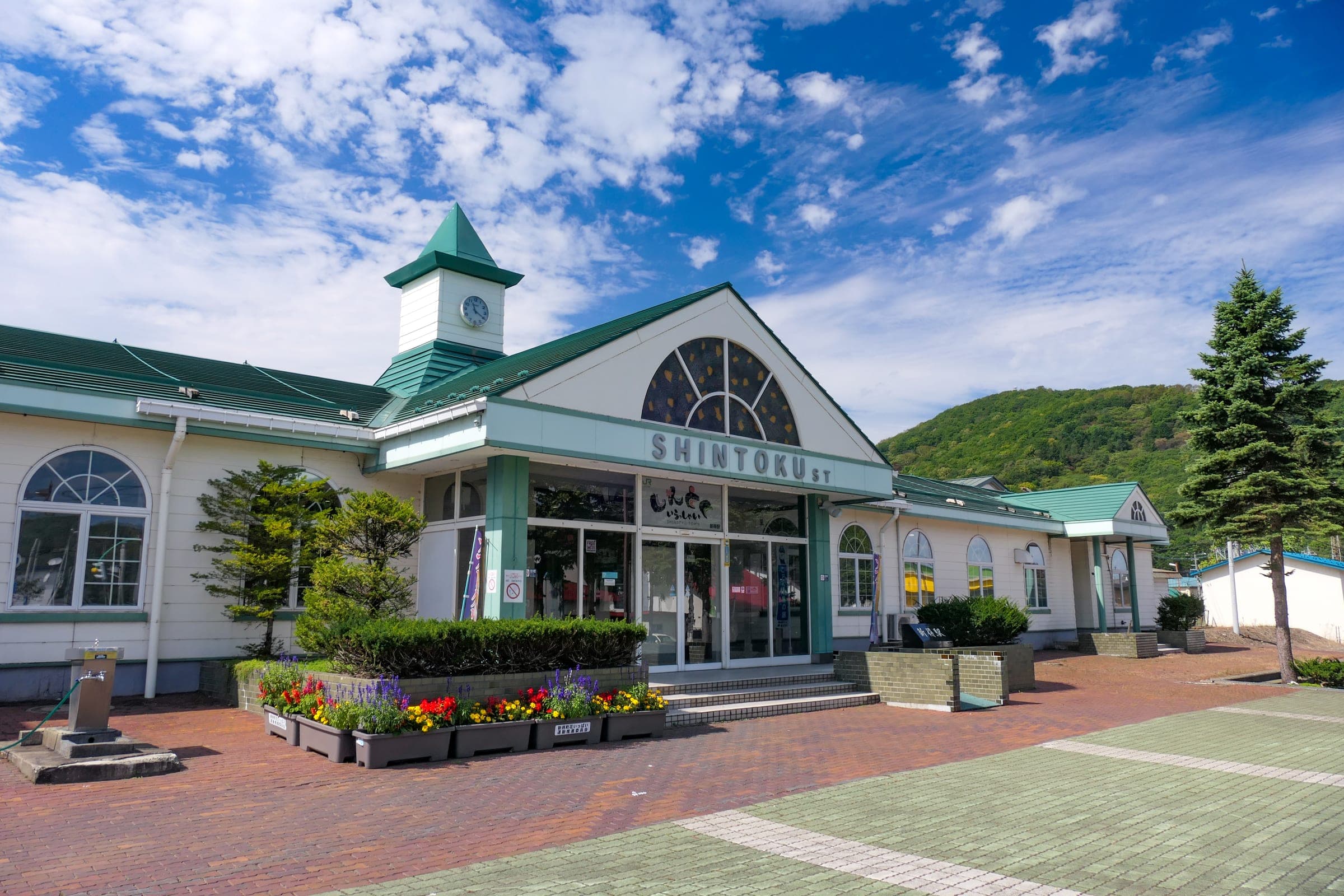 Flower beds line the front of Shintoku Station under its green roof and arched window
