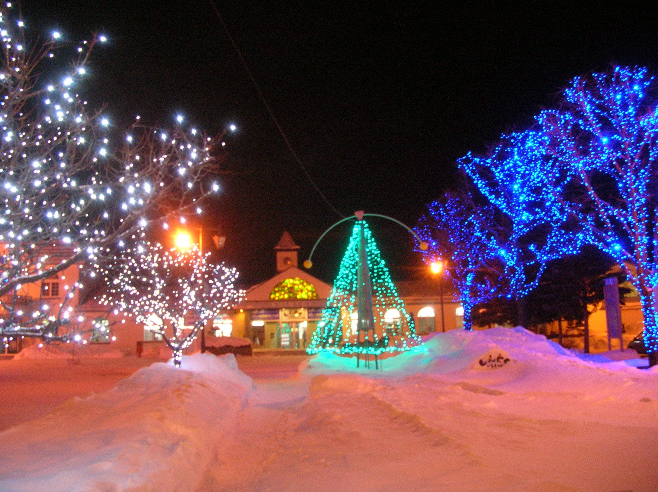 Blue and white lights glow over the snow in the square outside Shintoku Station