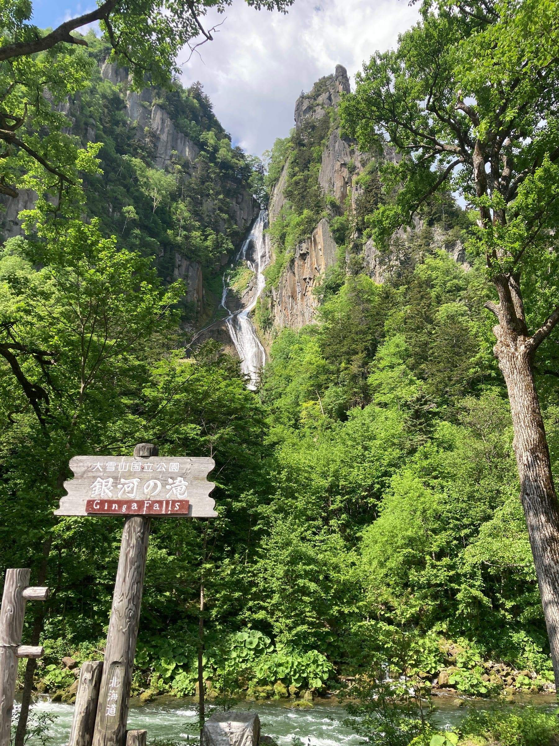 Ginga Falls drops down a forested cliff in Sounkyo behind its wooden sign