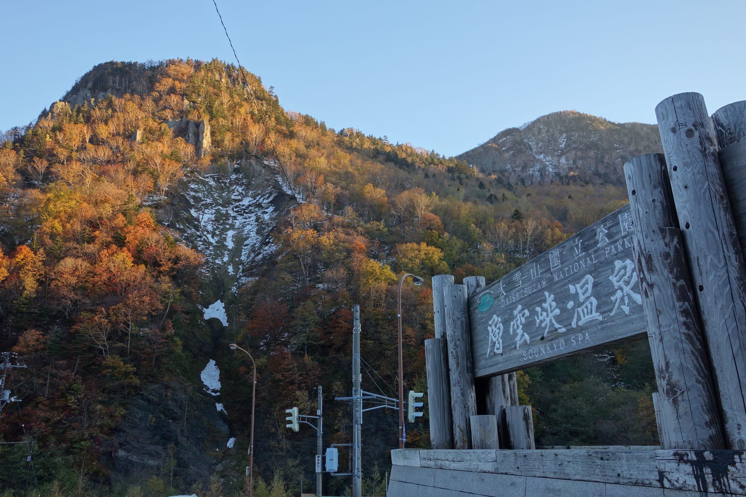Autumn colour covers the cliffs above the carved wooden gate of Sounkyo Onsen