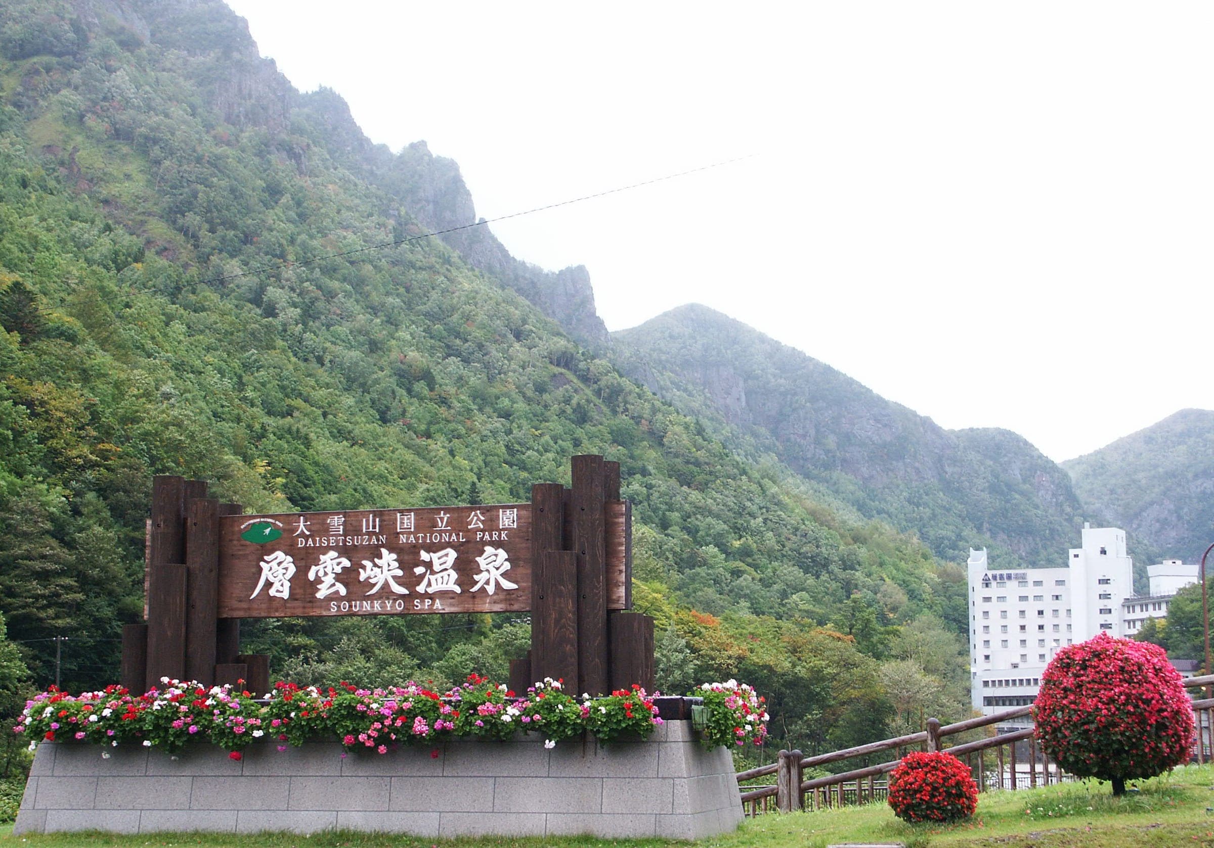 A carved sign welcomes visitors to Sounkyo Onsen beneath steep wooded cliffs