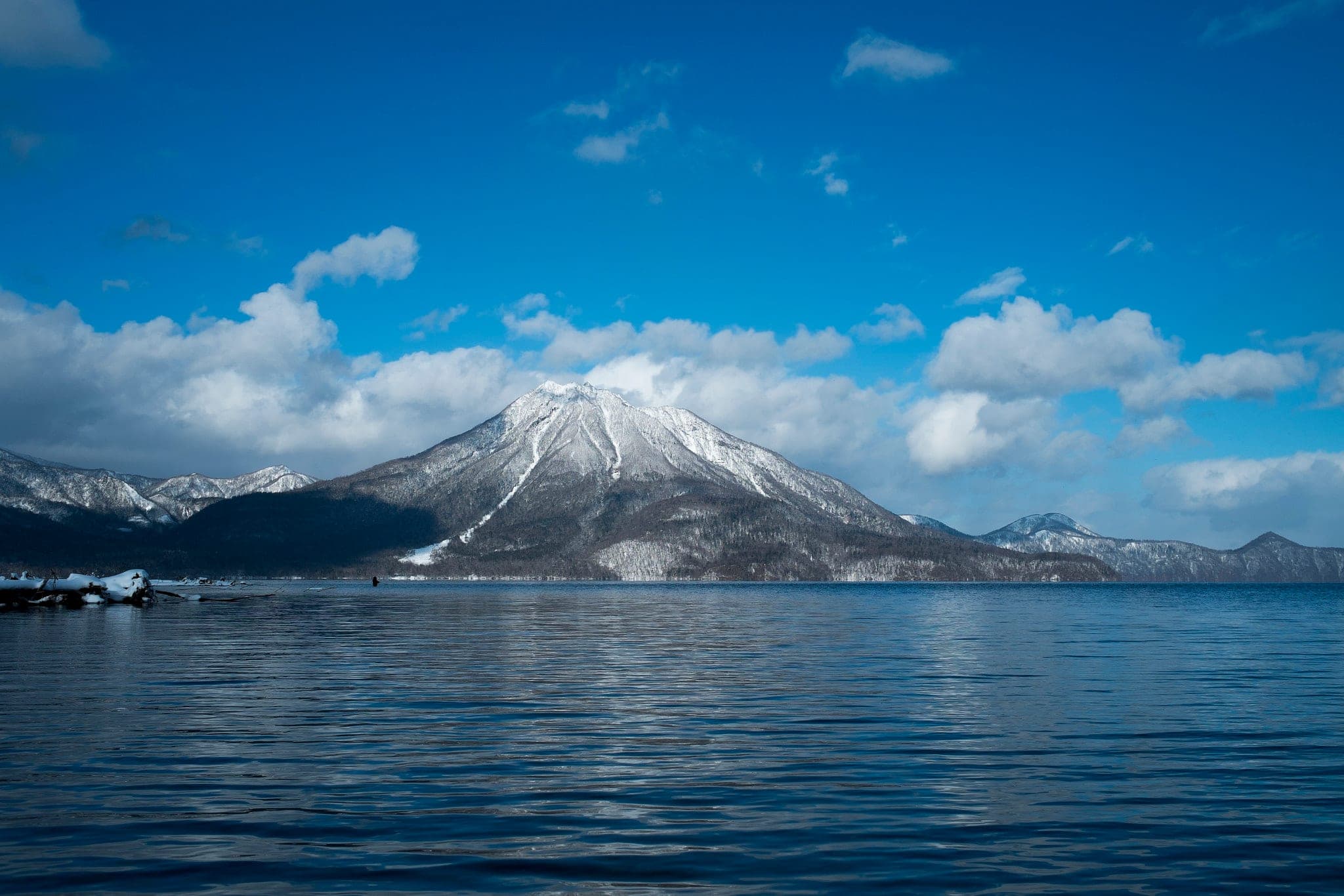 Snow covers Fuppushi-dake above the blue water of Lake Shikotsu on a clear winter day