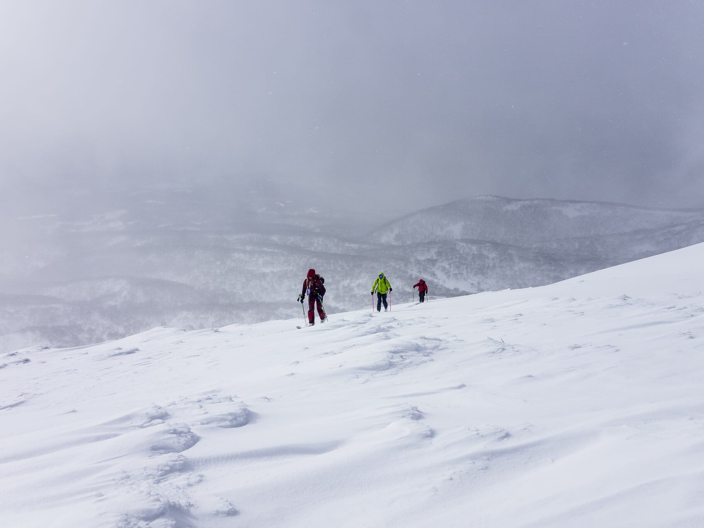 Three ski tourers climb the open upper slopes of Chisenupuri in flat light