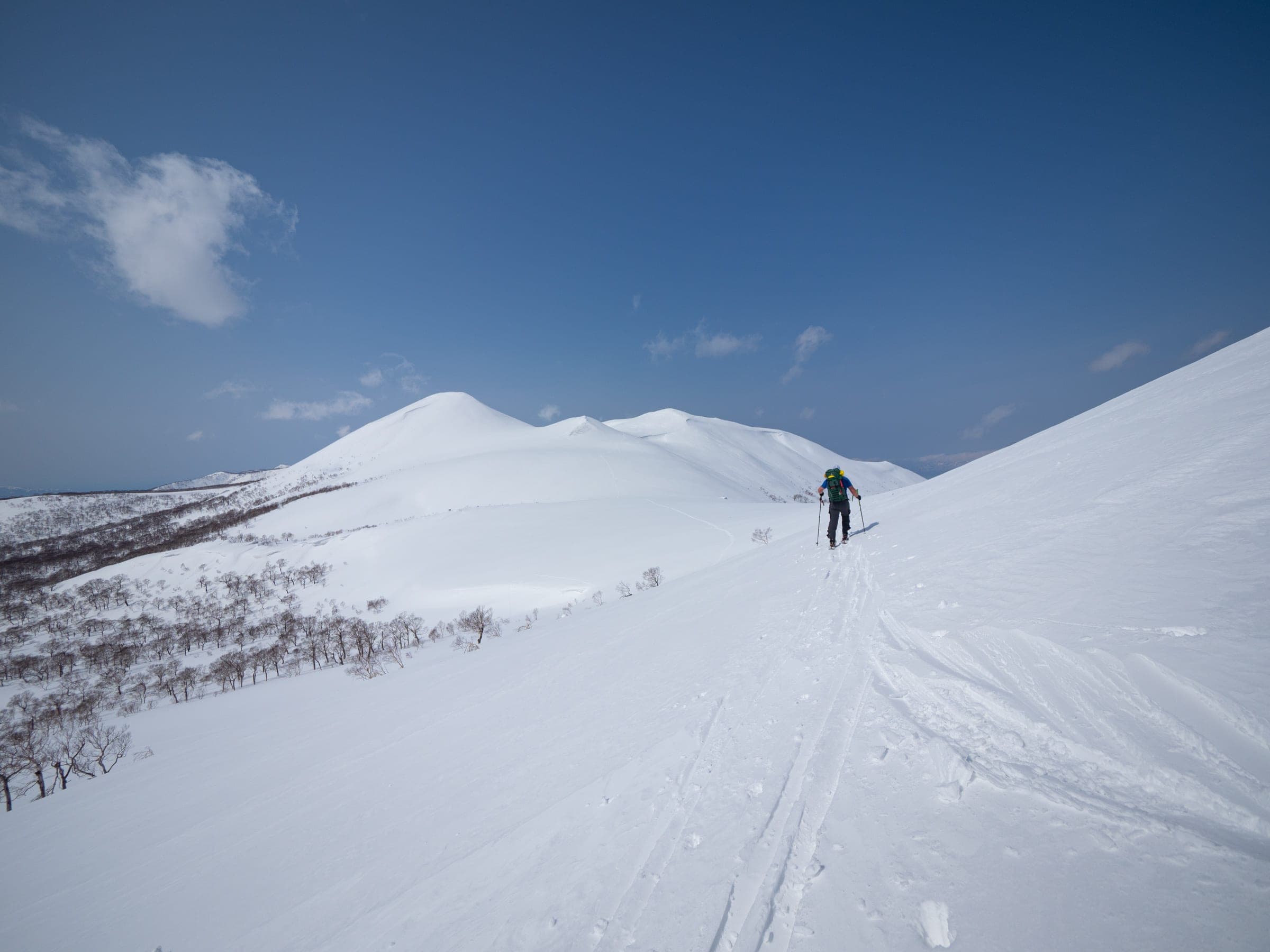 A ski tourer crosses an open shoulder on the Niseko Haute Route traverse