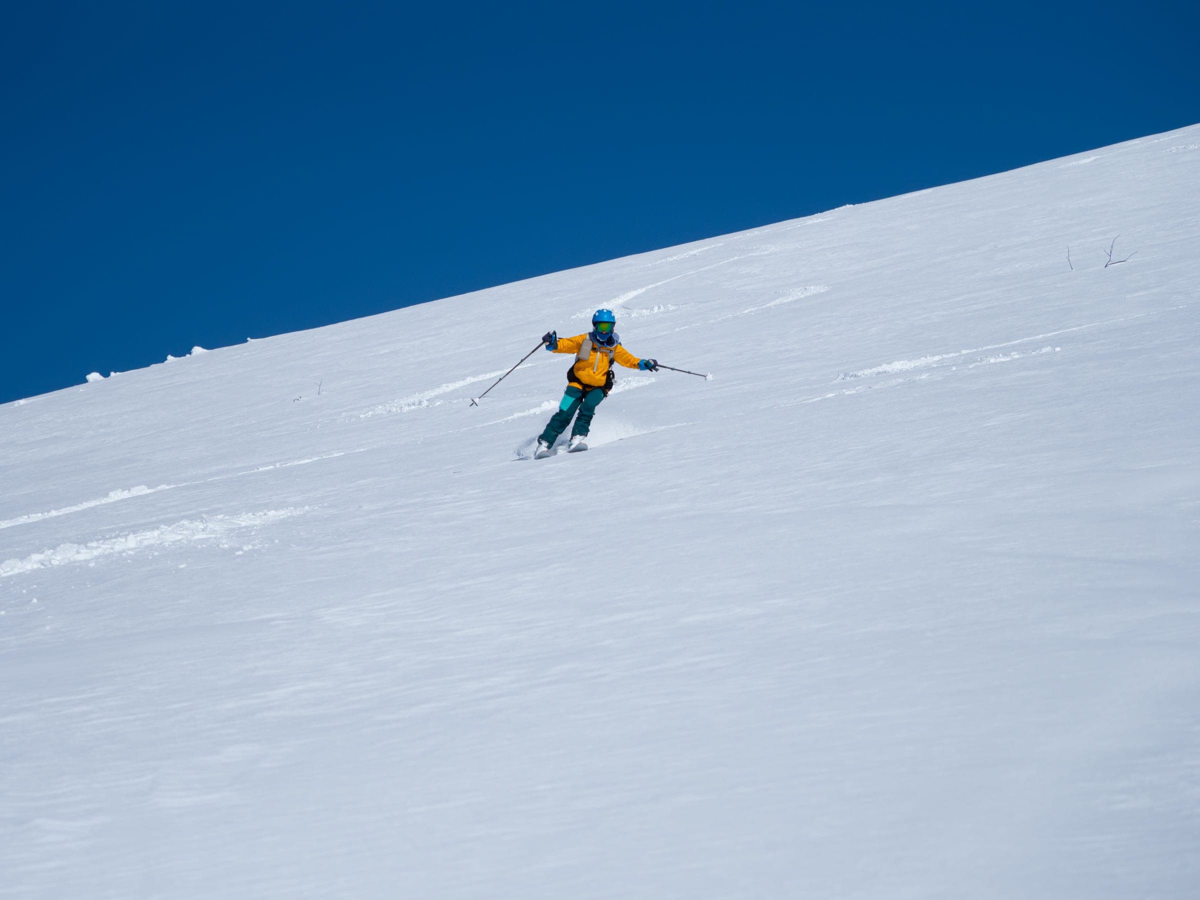 A skier in yellow carves down the open south face of Mekunnai-dake