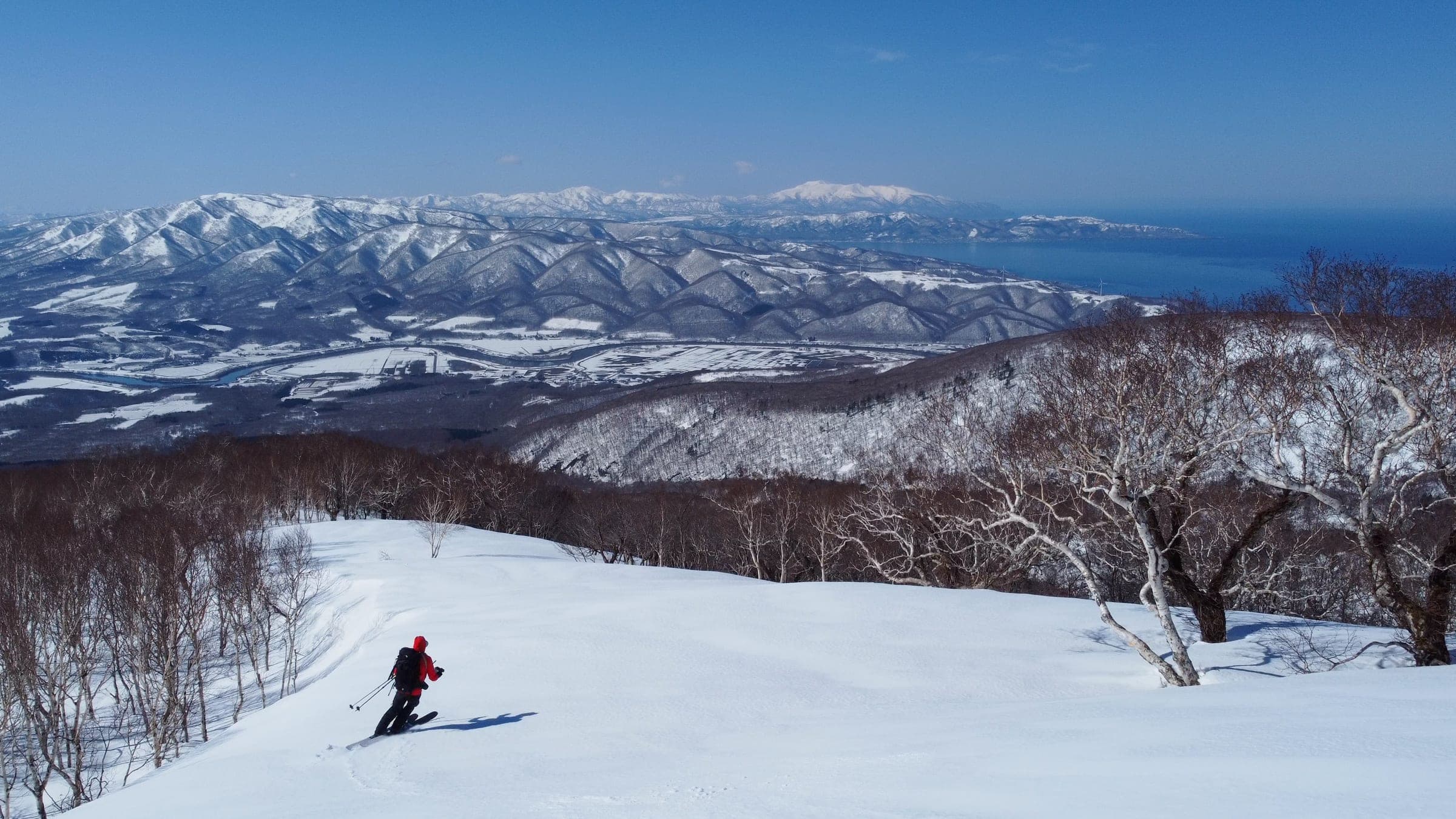 A skier descends the Sabo Dam route on Raiden-yama with the sea below