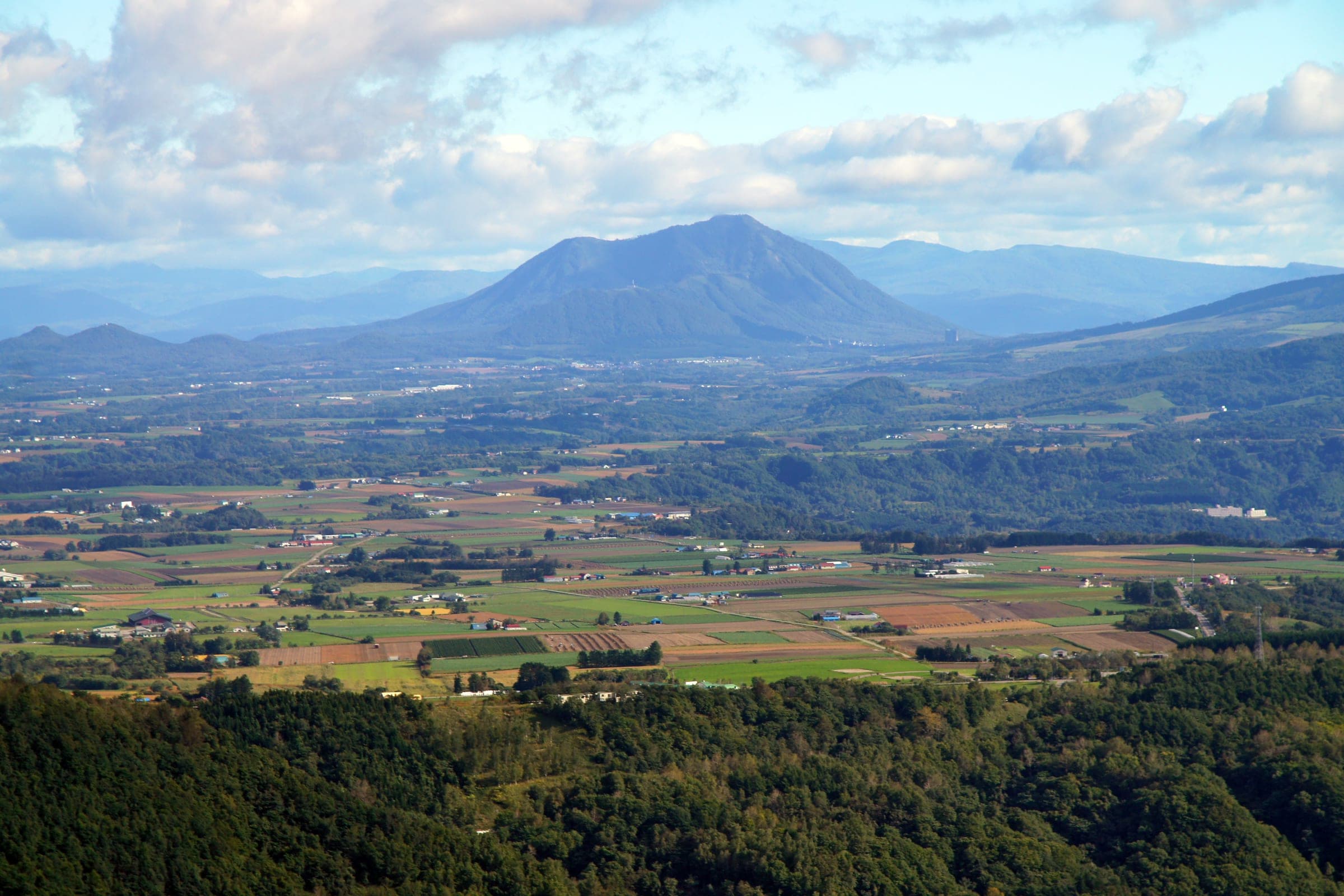 Shiribetsu-dake rises above farmland and forest seen from the hills by Lake Toya in autumn