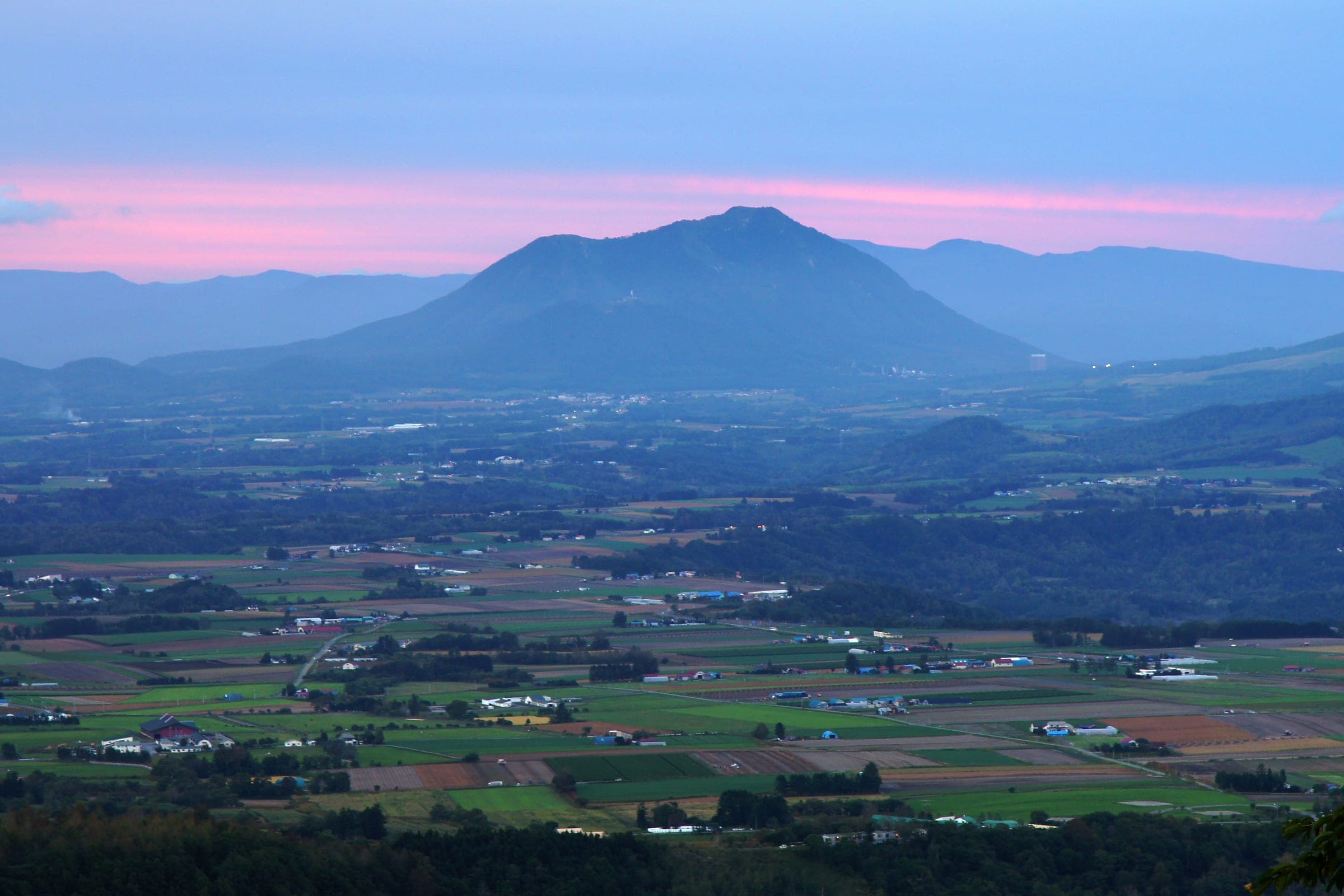 Shiribetsu-dake silhouetted under a pink dusk sky above the farmland below