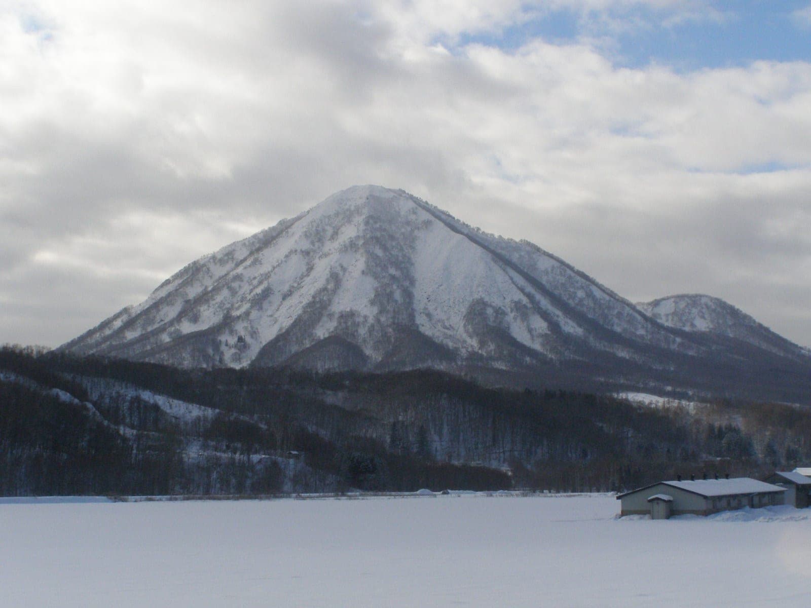 Fresh snow covers the cone of Shiribetsu-dake under a grey winter sky