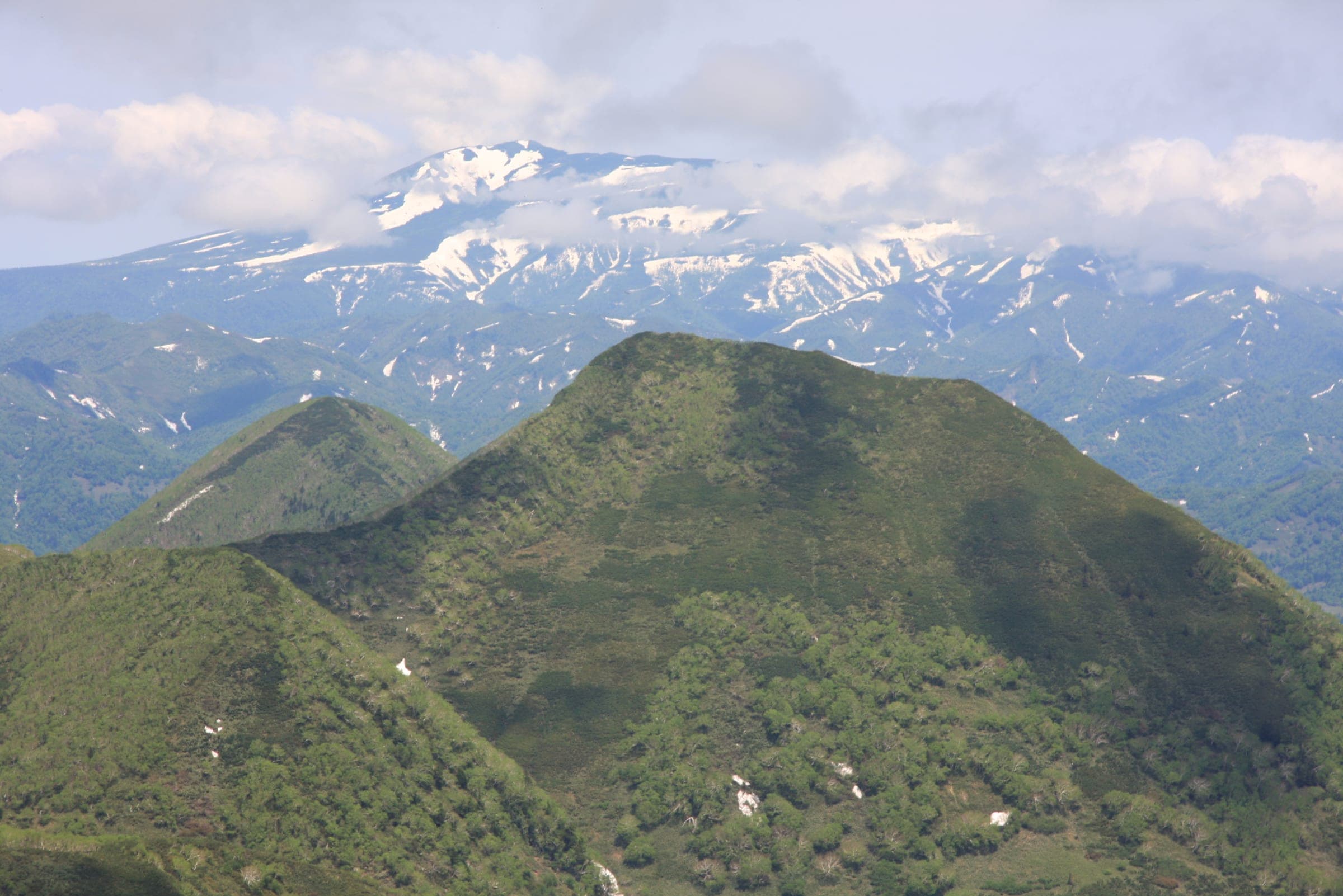 Snow-streaked Unabetsu-dake stands behind the green summit of Mount Musa in early summer