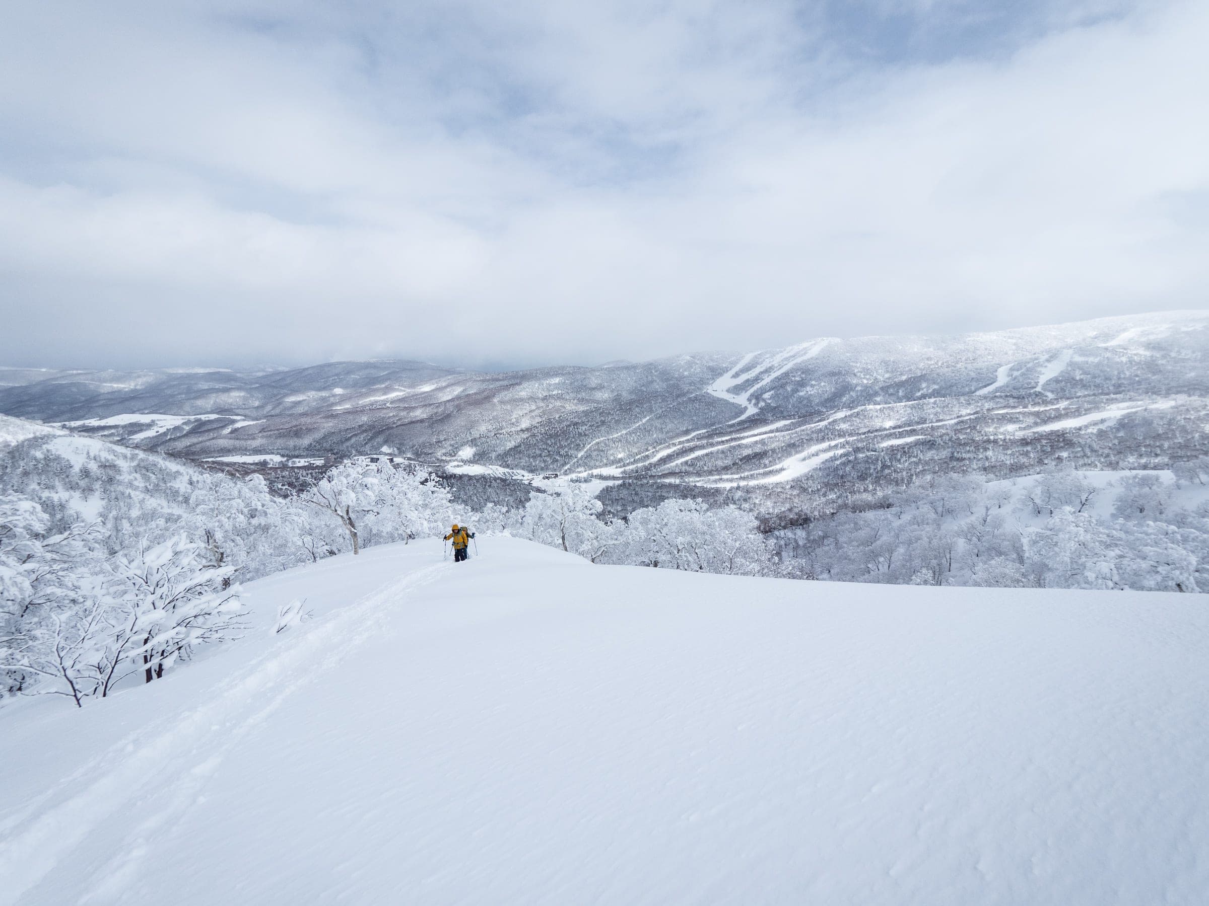 A ski tourer stands on the 1107 m peak above Kiroro with snowy ridges beyond