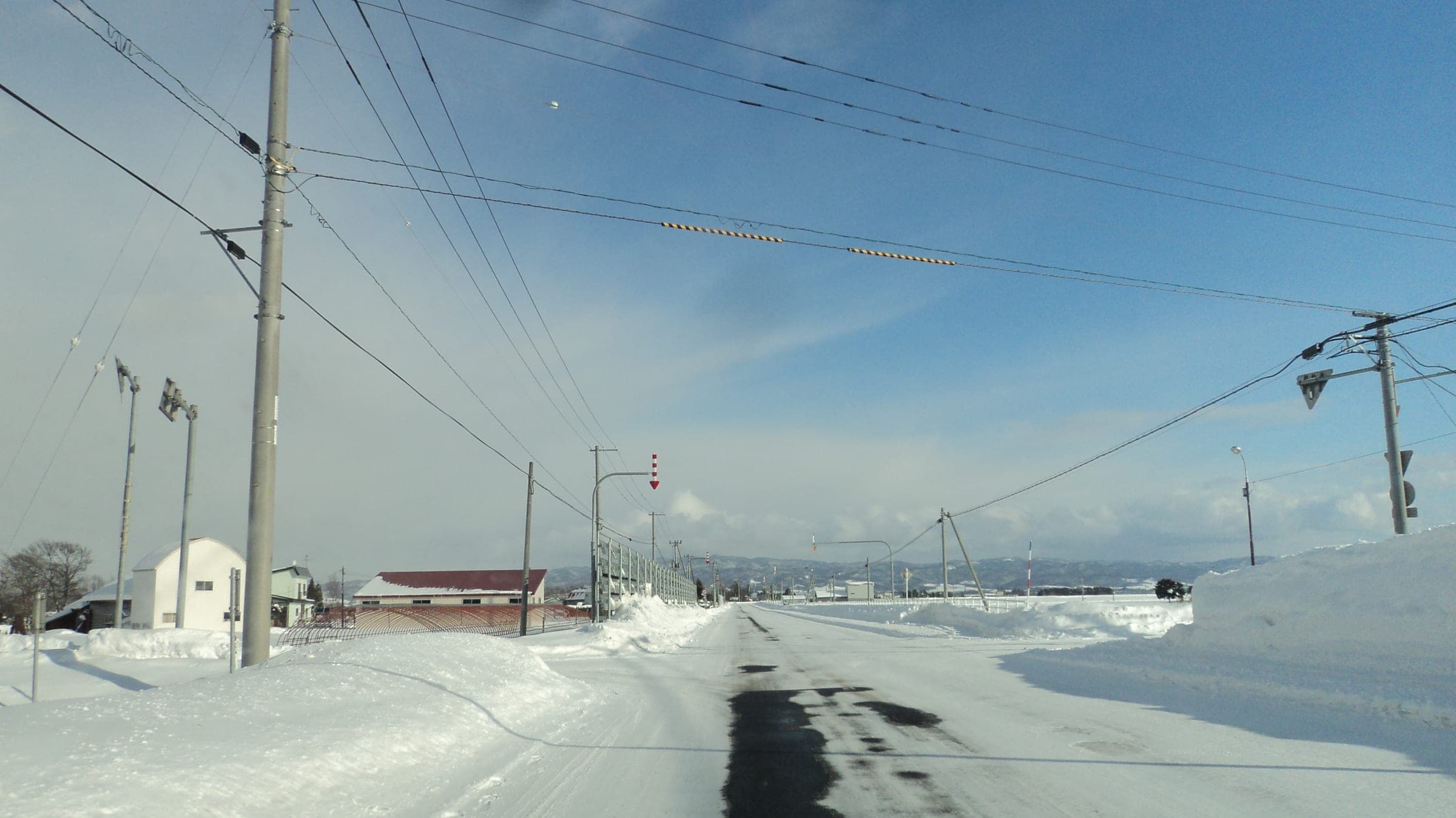 Arrow markers hang over a snow-packed rural road in Hokkaido to show drivers the edge