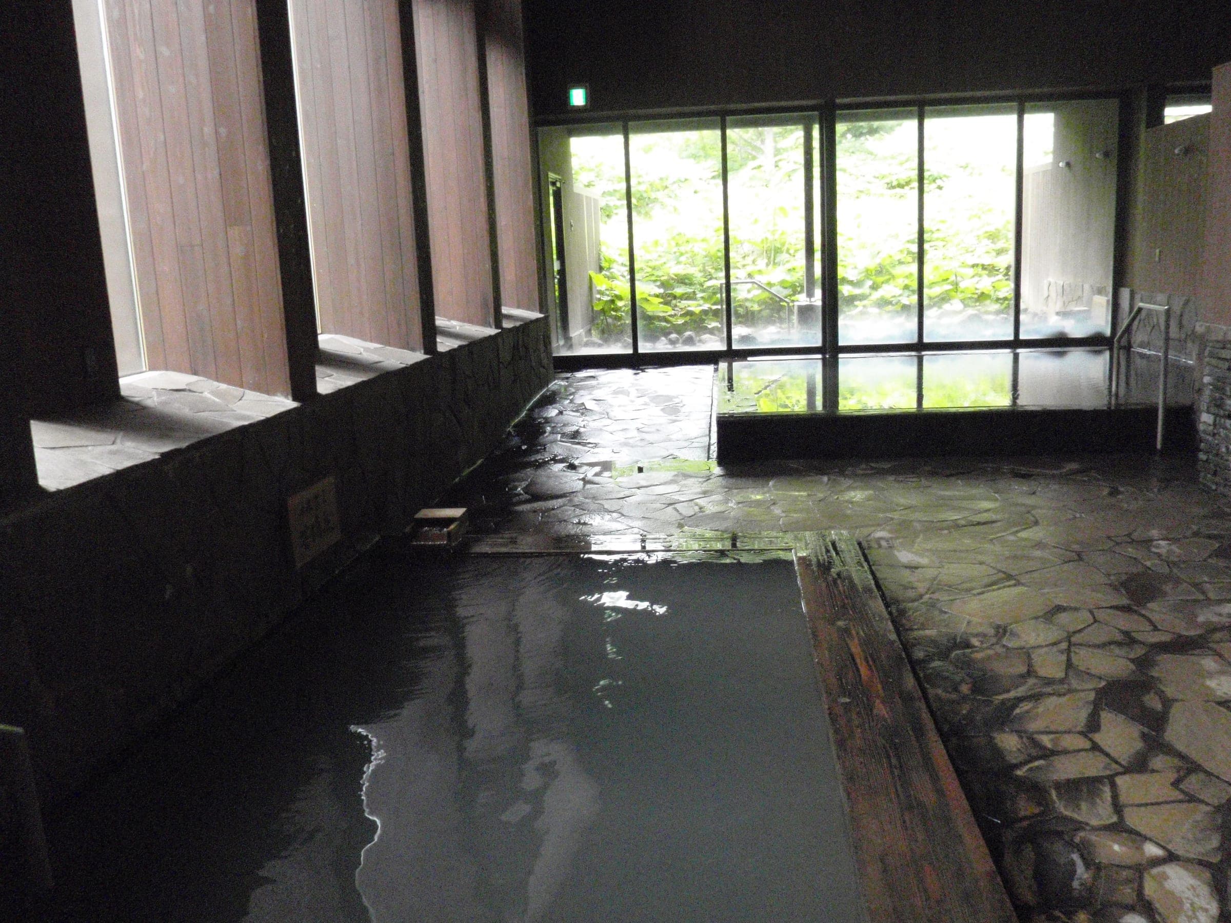 Stone floor and a wooden-edged pool in the indoor bath at Yukomaso, Asahidake Onsen