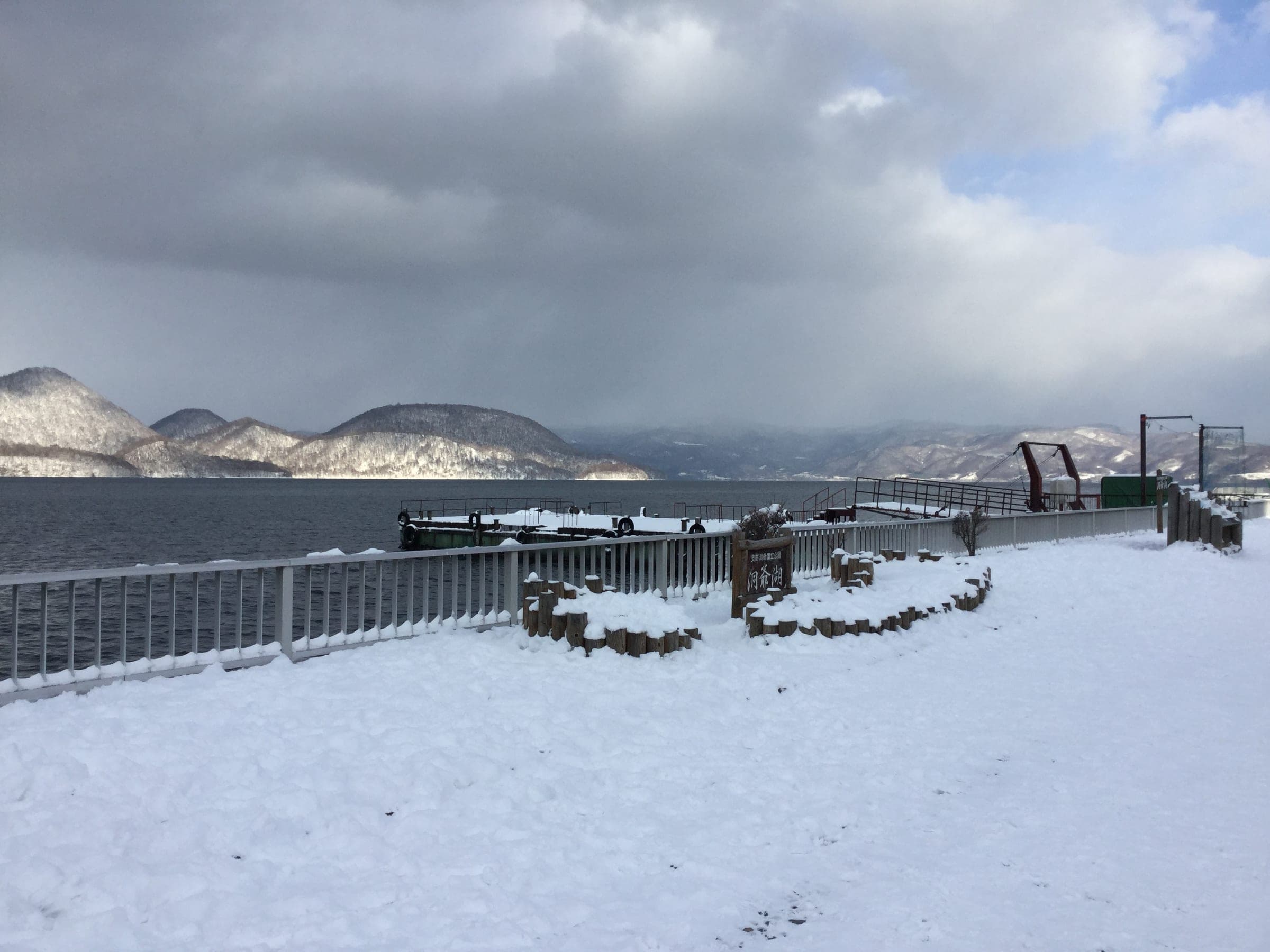 Snow covers the Toyako Onsen lakeshore as clouds hang over Nakajima on Lake Toya