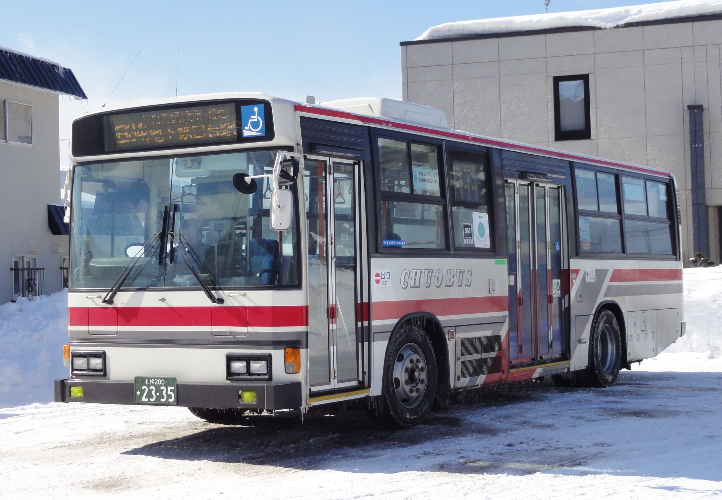 A red and white Hokkaido Chuo Bus coach waits beside snowbanks