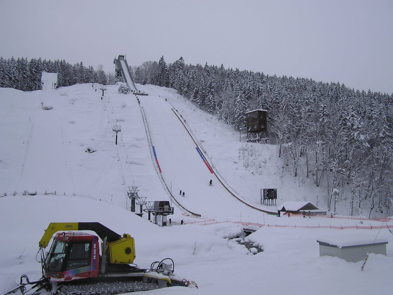 A snowcat grooms below the Piyashiri ski jump as snow-laden forest lines the hill at Nayoro